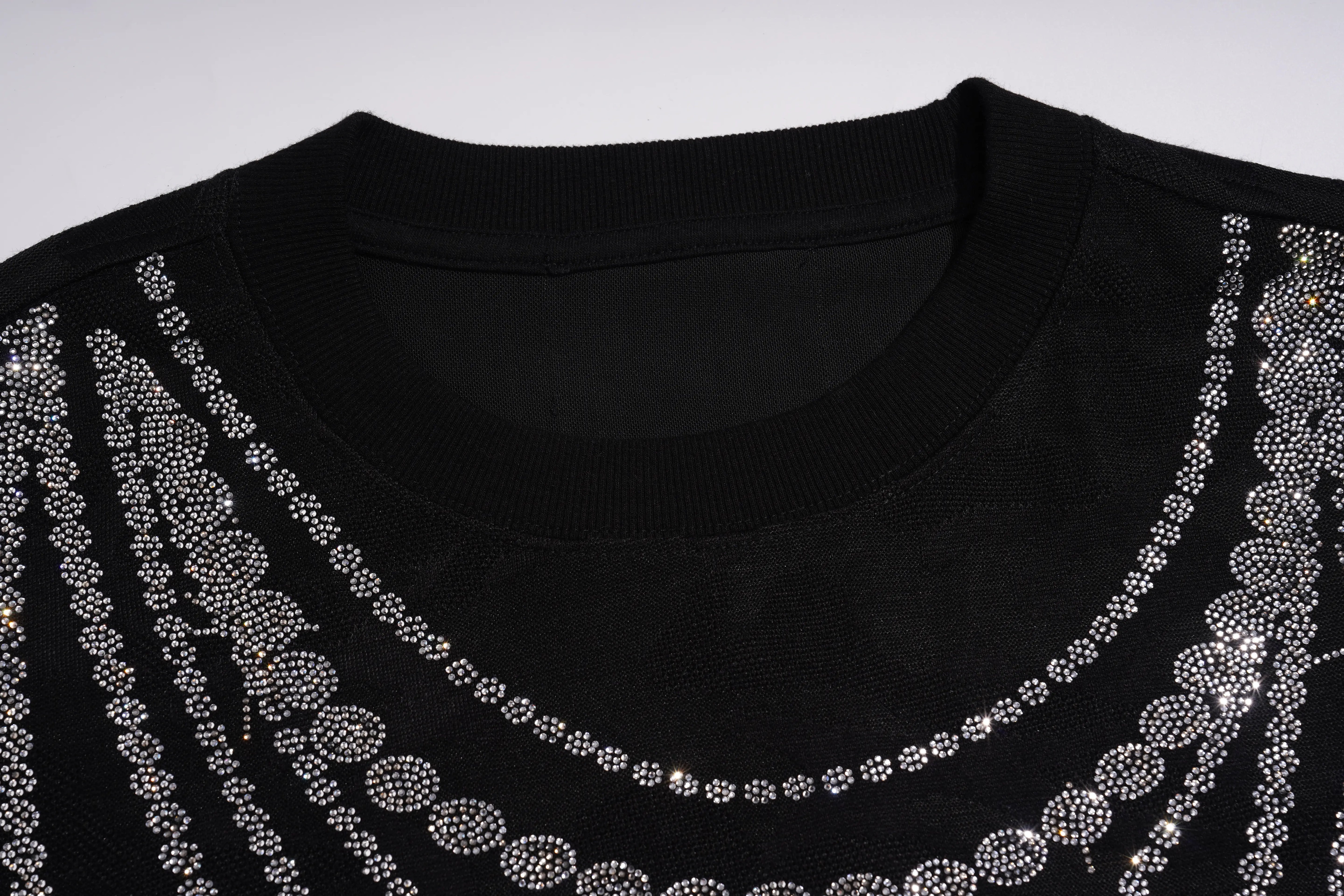 Close-up of a black crewneck sweater decorated with rows of silver rhinestones forming circular and vertical patterns around the neckline. TCH Rhinestone Teddy Bear Pearl Chain Graphic Sweatshirt