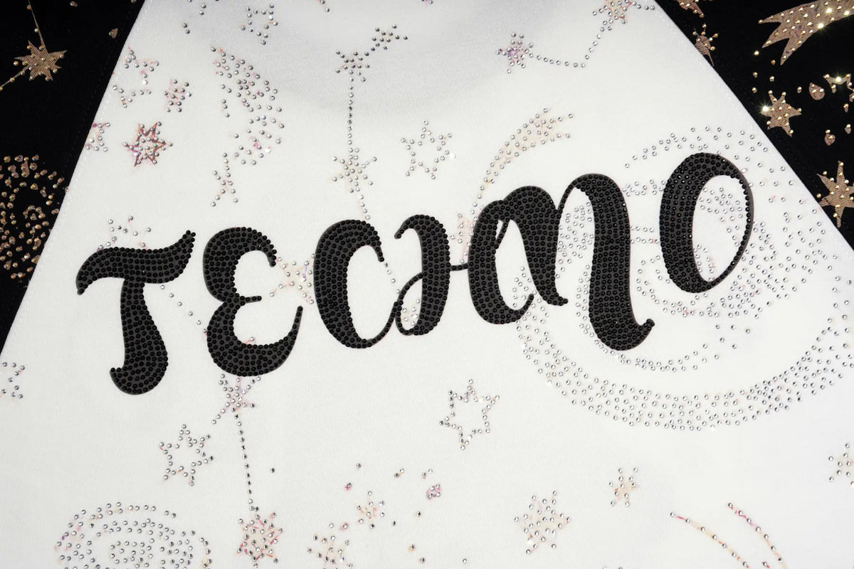A close-up of a white fabric item, likely a bandana or scarf, featuring the word 'TECHNO' spelled out in black rhinestone lettering. The fabric is decorated with small rhinestone star and swirl patterns, and is shown against a dark background with gold star details. TCH Rhinestone Teddy Bear Techno Raglan T-Shirt