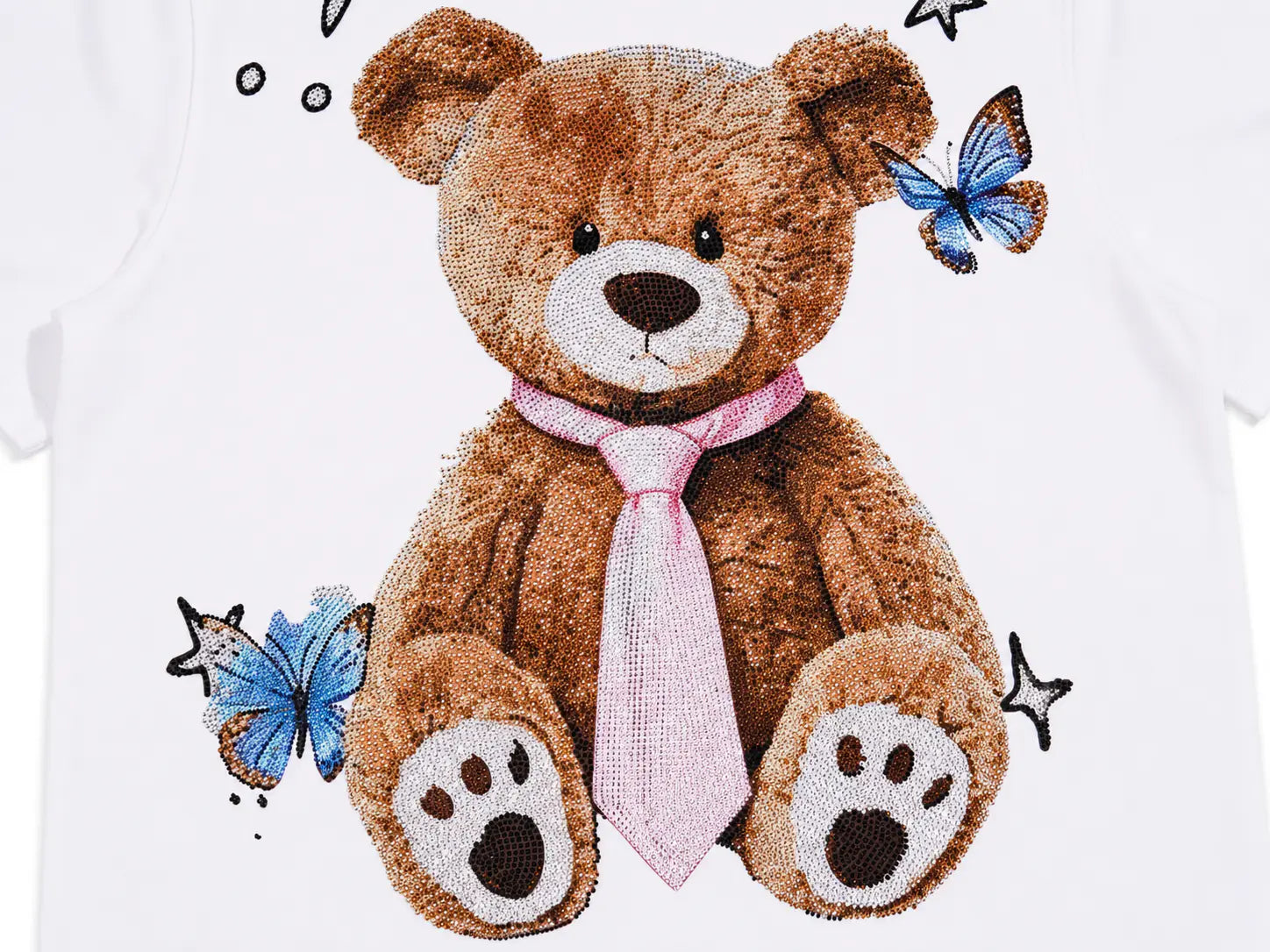 A close-up of a white garment featuring a large teddy bear graphic in brown with a pink tie, plus blue butterflies and small black star details. TCH Rhinestone Teddy Bear White T-Shirt