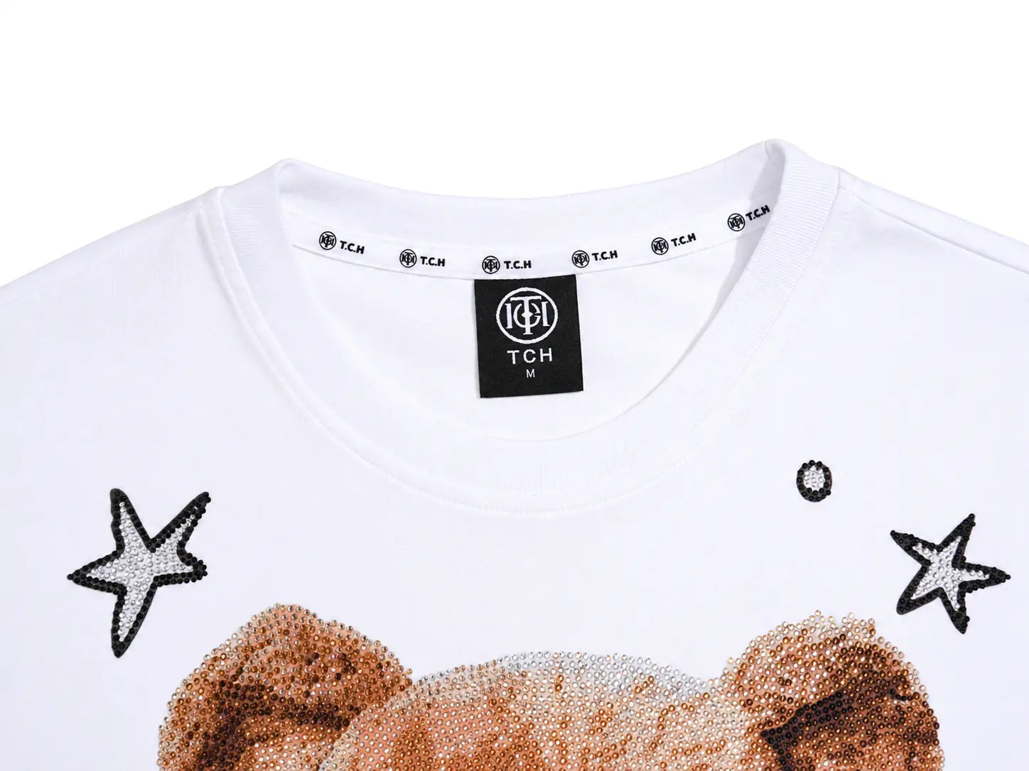 Close-up of a white T-shirt with a teddy bear graphic and sequined star details, showing the neck label with TCH branding. TCH Rhinestone Teddy Bear White T-Shirt