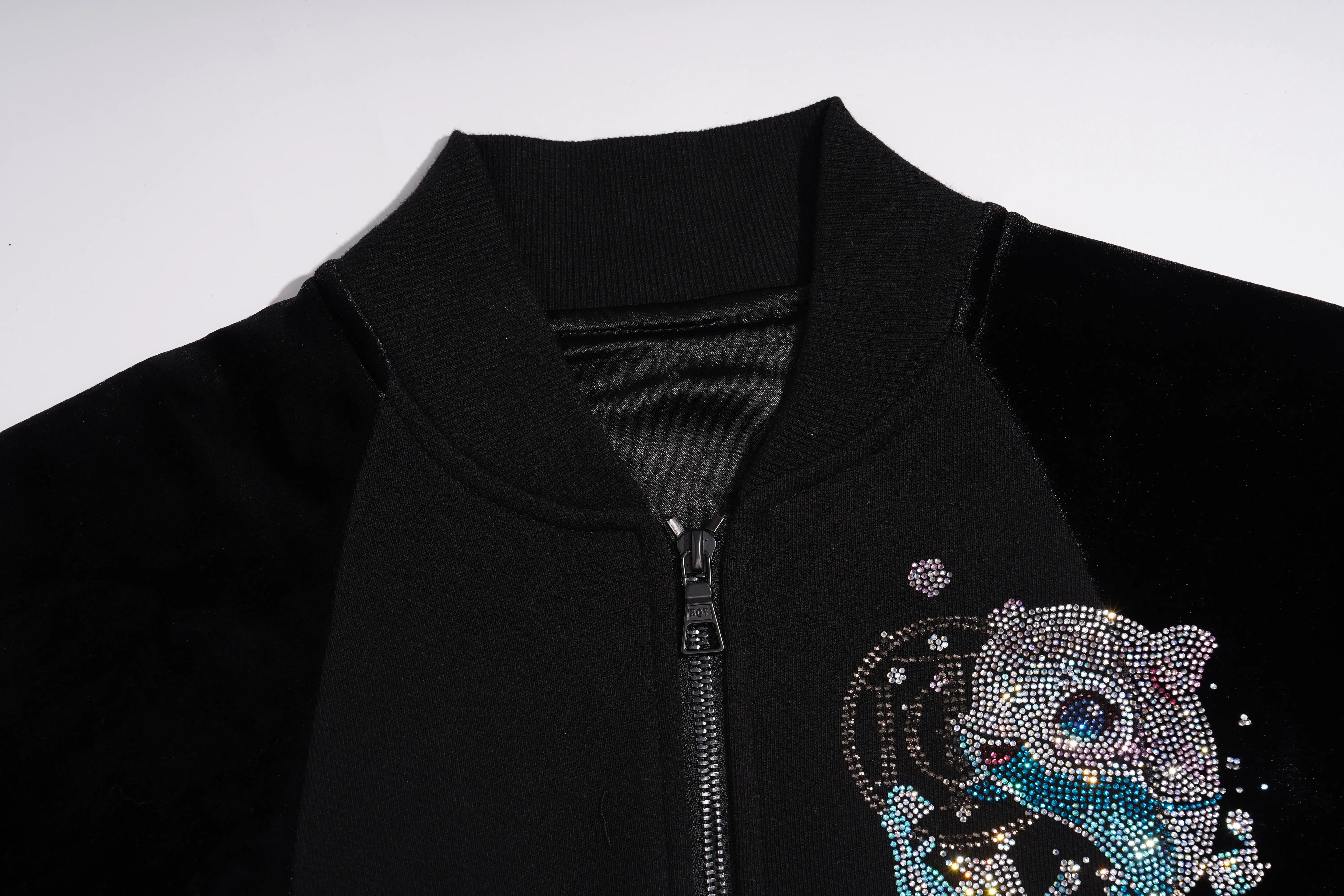 Close-up of a black zip-front jacket with a ribbed collar and a large rhinestone embellished animal graphic on the lower right side, shown against a plain light background. TCH Rhinestone Teddy Bear Wing Sleeve Bomber Jacket