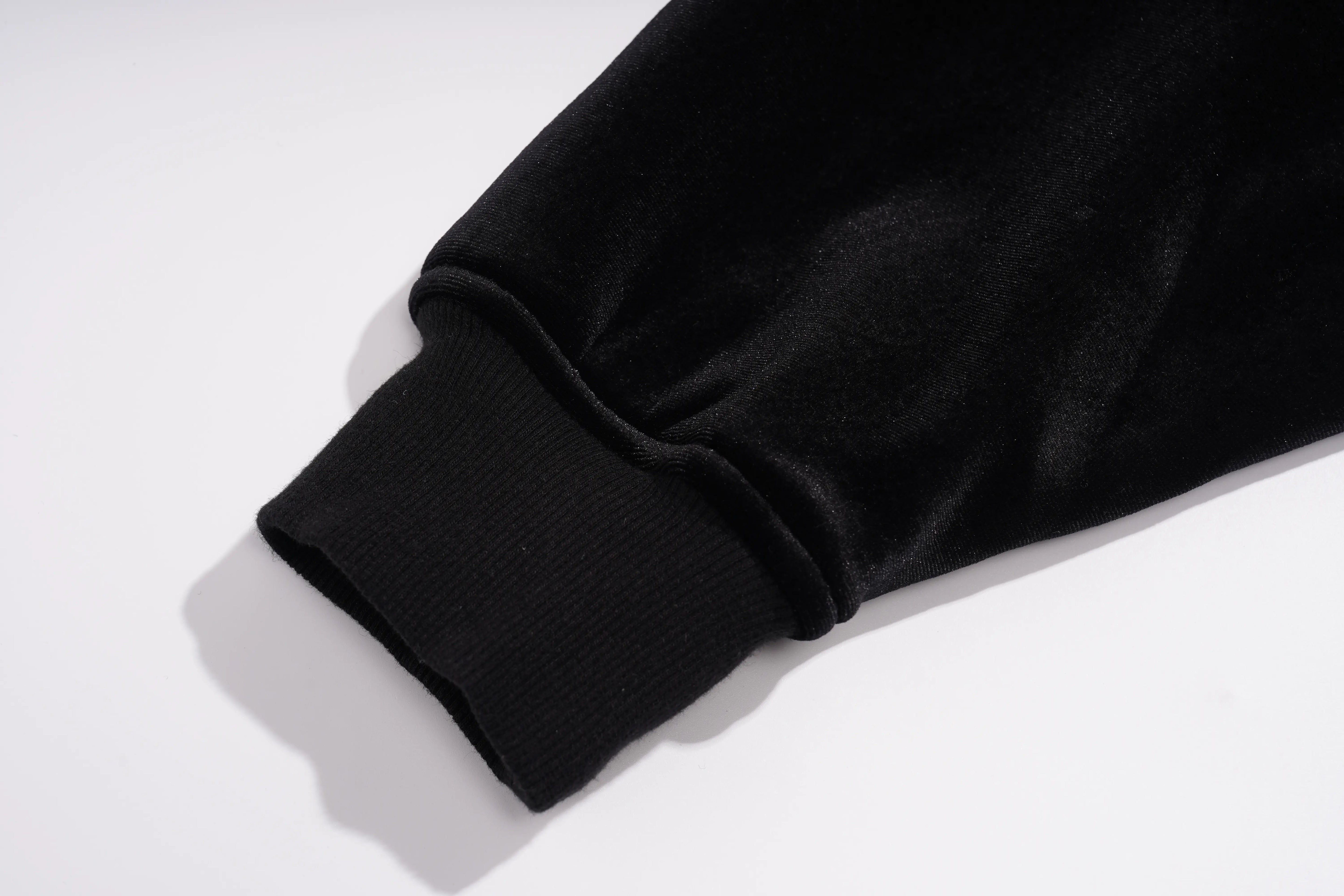 Close-up of a black ribbed knit cuff on a black fabric garment, photographed on a clean white background. TCH Rhinestone Teddy Bear Wing Sleeve Bomber Jacket