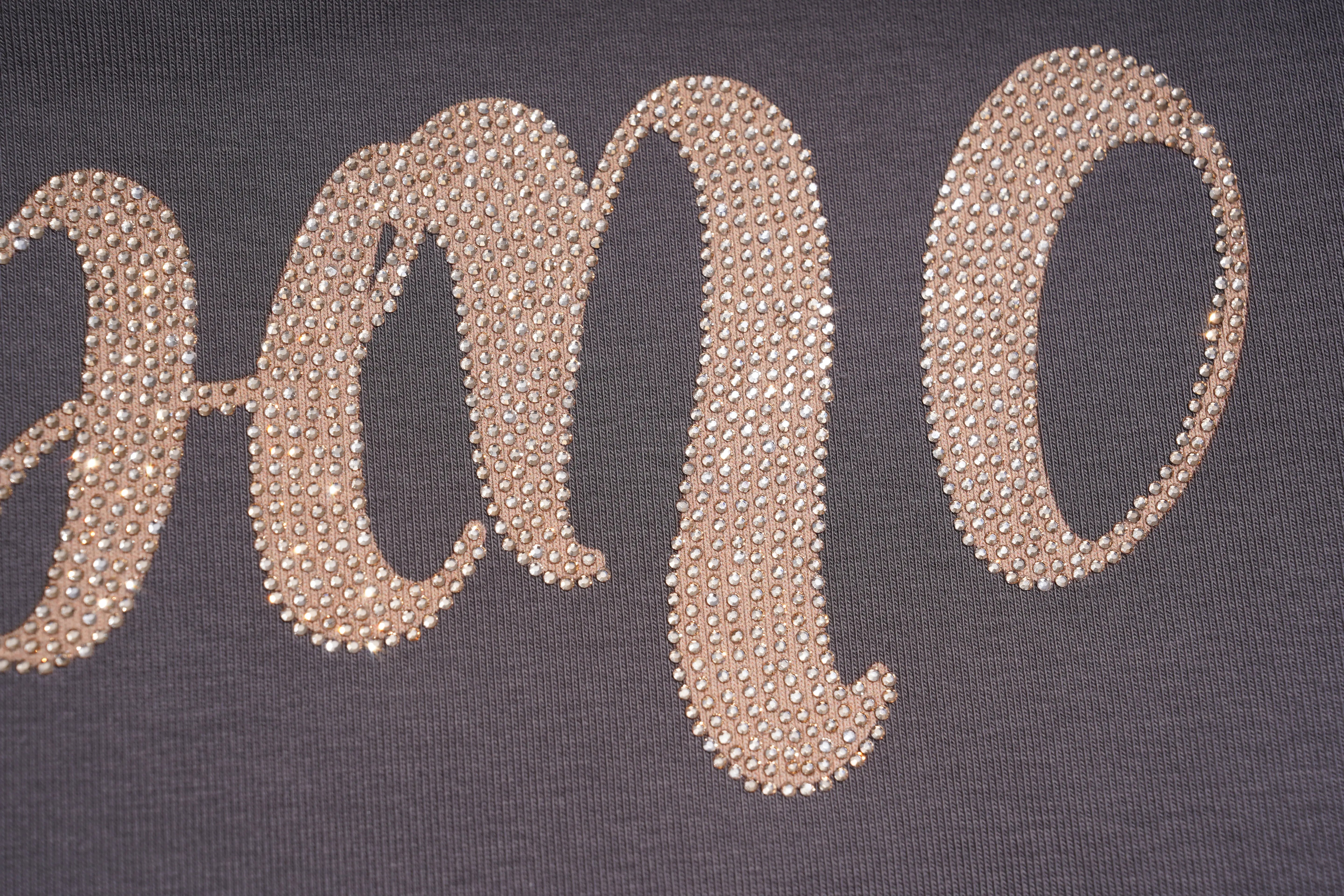 A close-up of a dark gray knit garment featuring a large script letter 'O' embellished with shimmering gold rhinestones. TCH Rhinestone Unicorn Graphic Charcoal T-Shirt