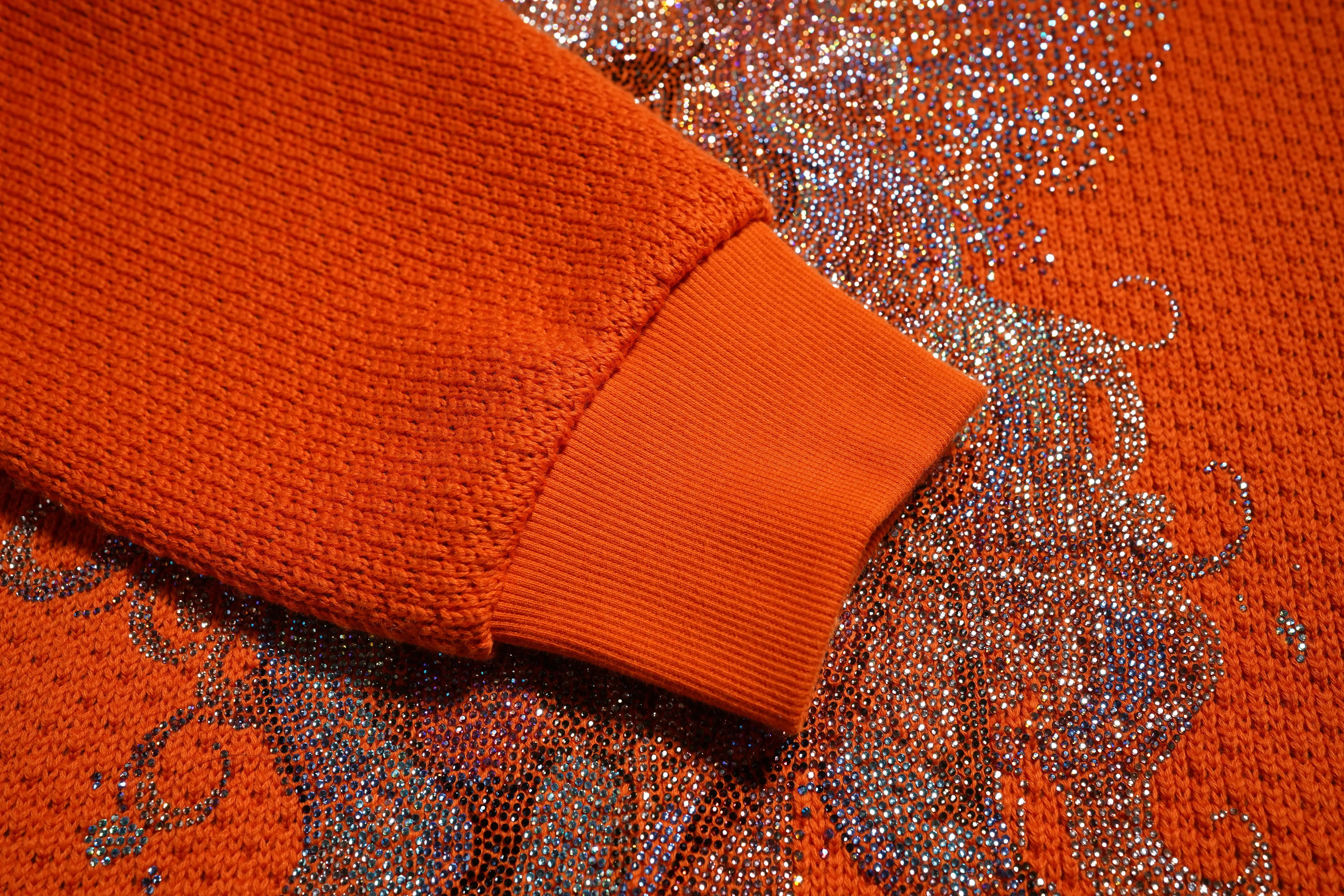 Close-up of an orange sweater with a decorative pattern on a matching background, TCH Rhinestone Unicorn Orange Hoodie