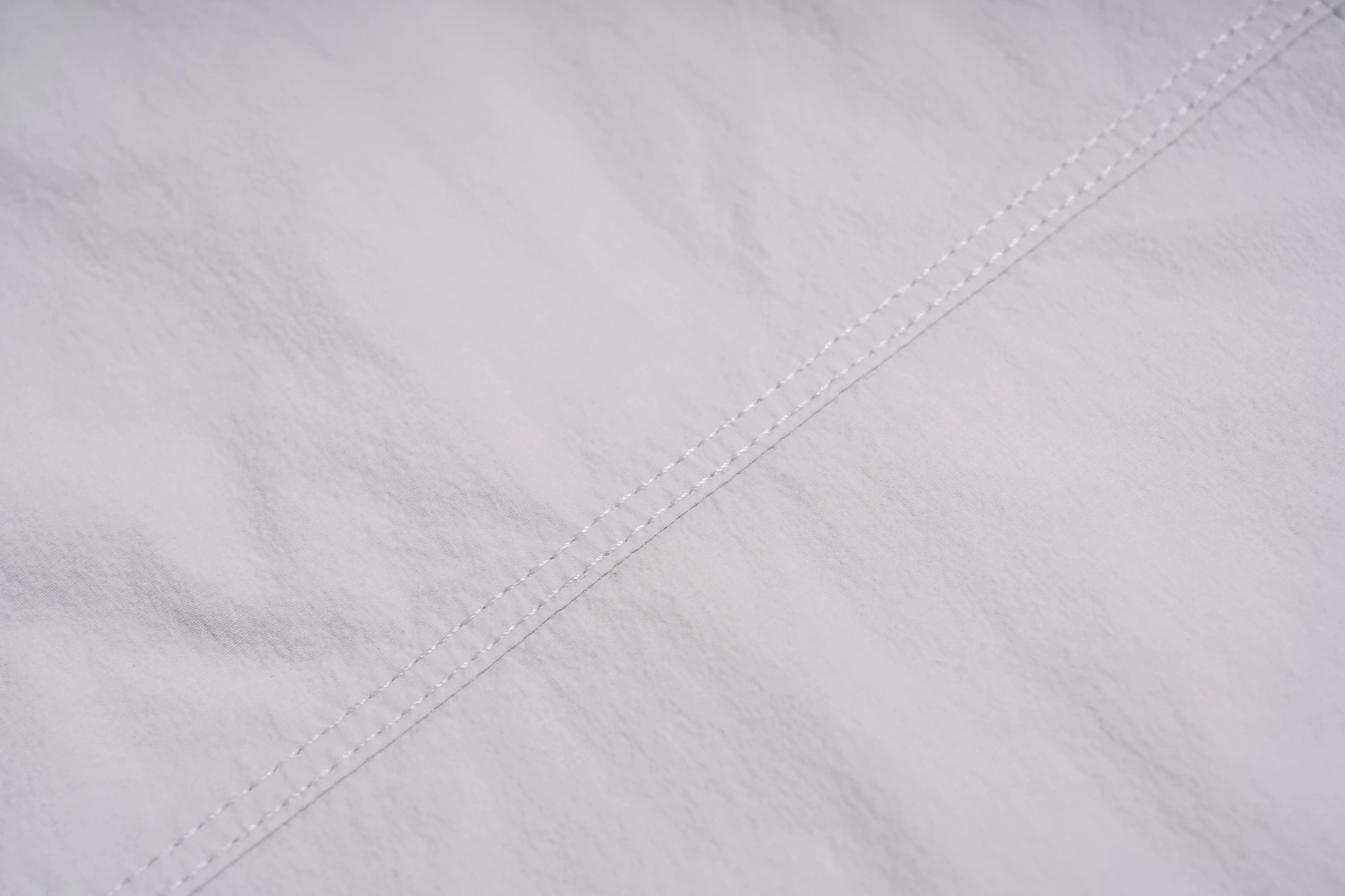 Close-up of a white textured fabric with a diagonal double-stitched seam. TCH Rhinestone Wing Active 3-Piece Tracksuit Set