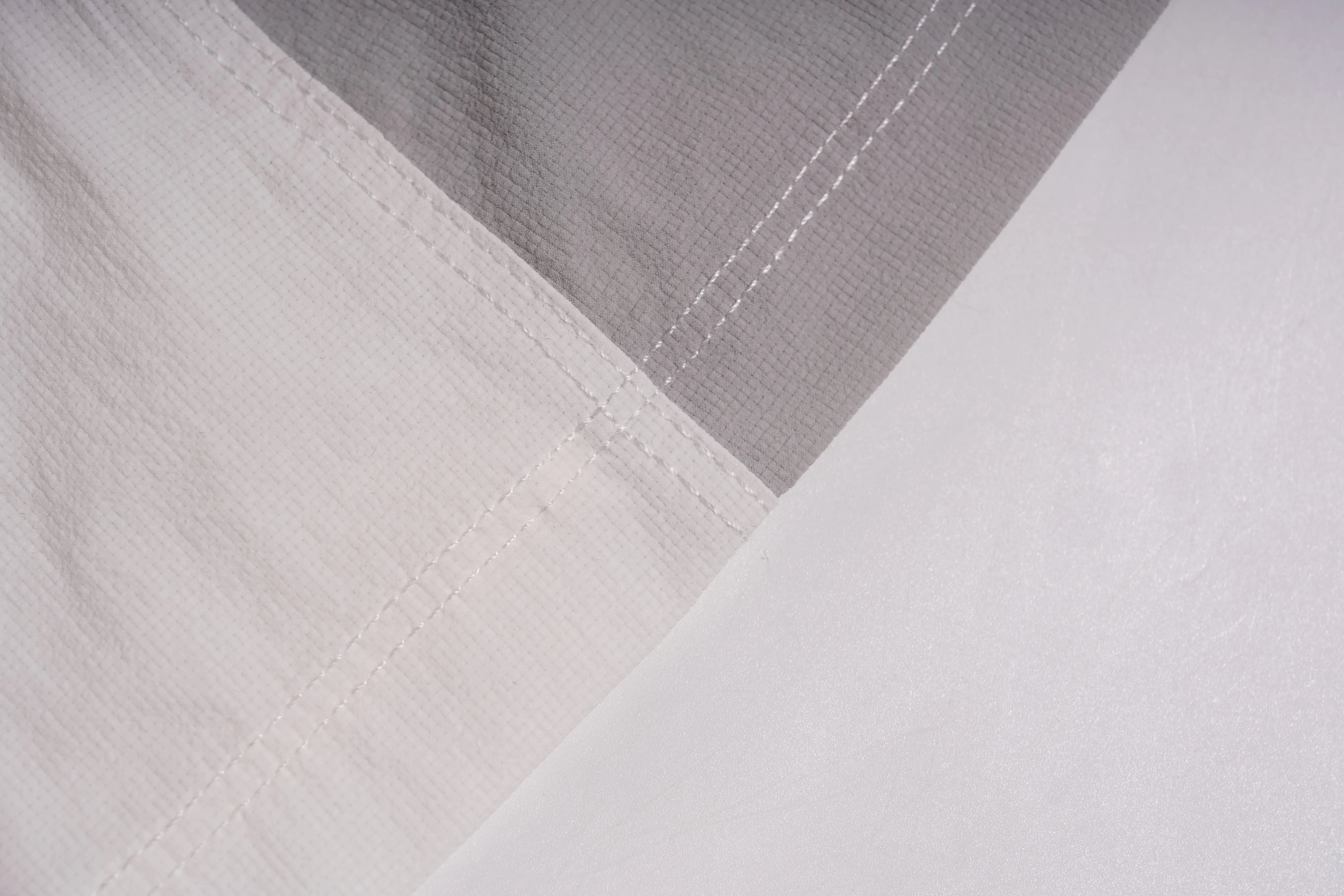 Close-up of a white fabric product, likely bedding such as a duvet cover or comforter, showing a folded corner that reveals a contrasting light gray inner layer with matching white stitching. TCH Rhinestone Wing Active 3-Piece Tracksuit Set