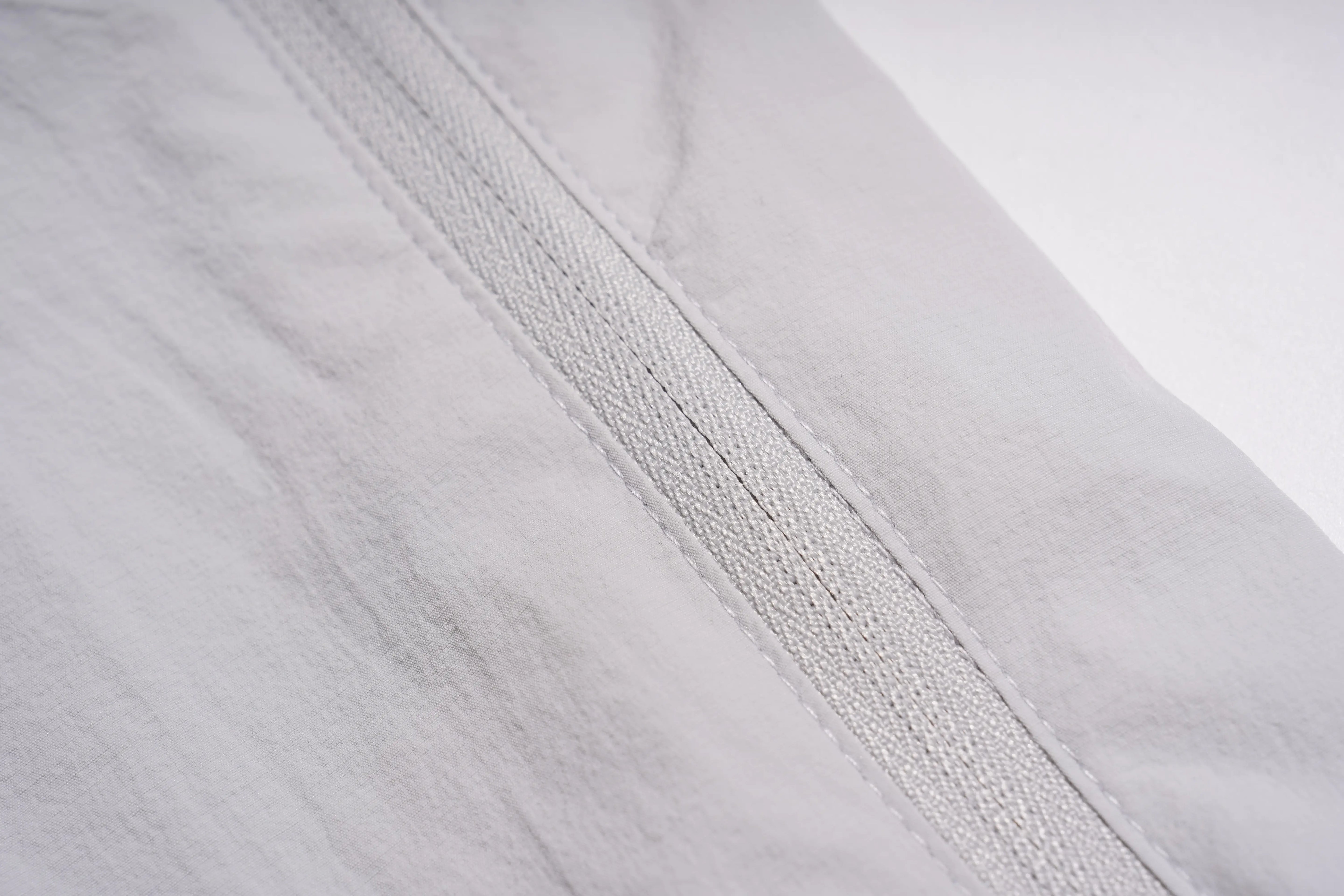 Close-up detail of a light gray fabric garment showing a diagonal seam and fine woven texture. TCH Rhinestone Wing Active 3-Piece Tracksuit Set
