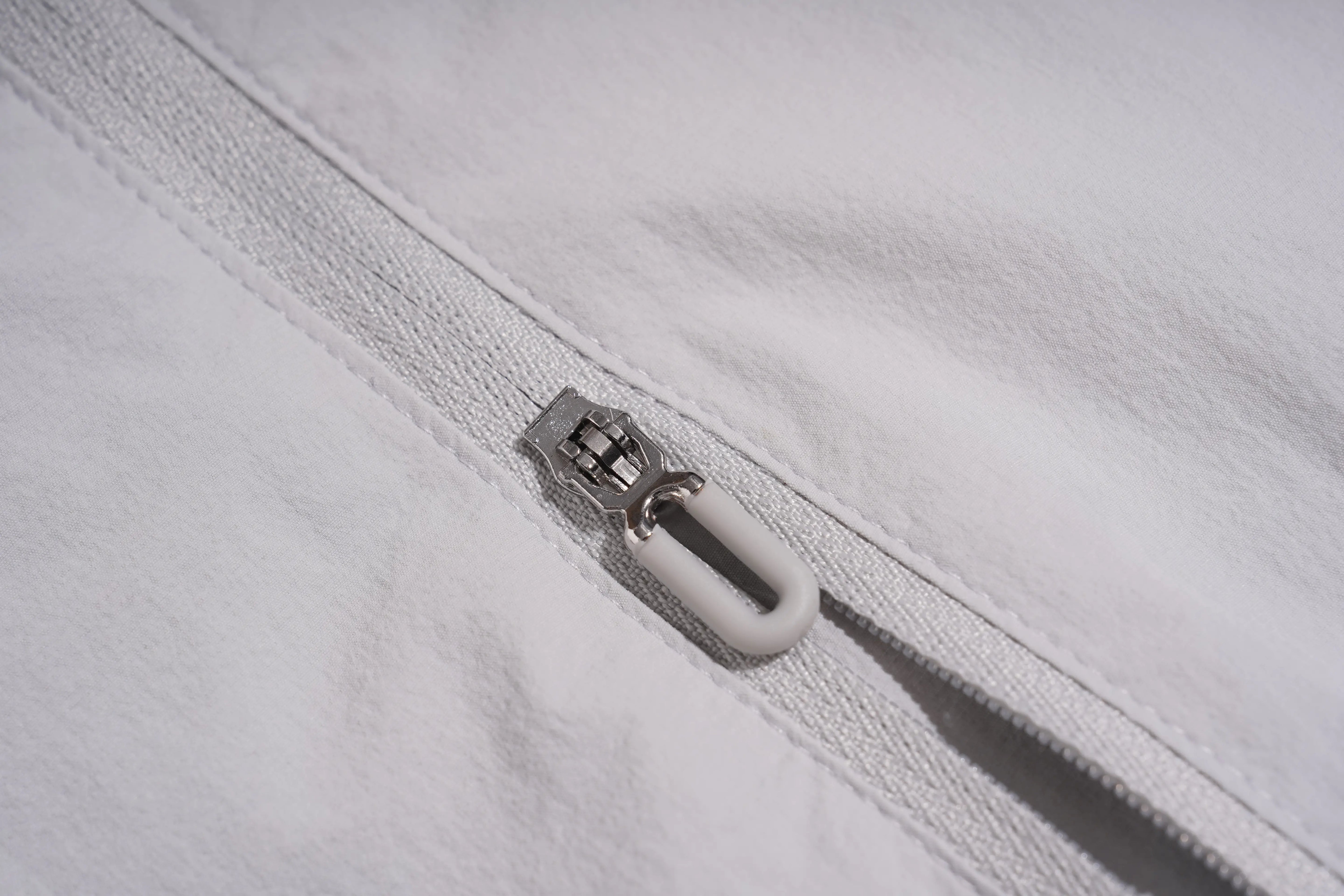 Close-up of a white fabric zipper with a white pull tab and a silver metal slider, showing the texture of the material. TCH Rhinestone Wing Active 3-Piece Tracksuit Set