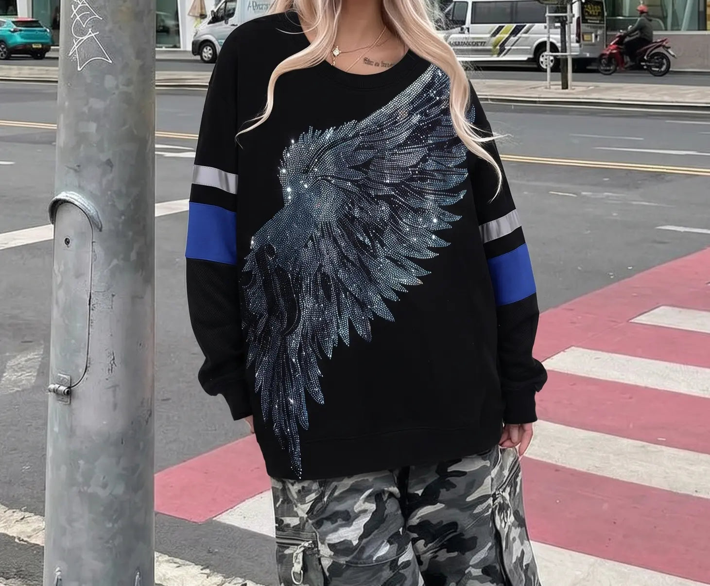 Person wearing a black sweater with a large blue feather design on a city street. TCH Rhinestone Wing Black Crewneck Sweatshirt