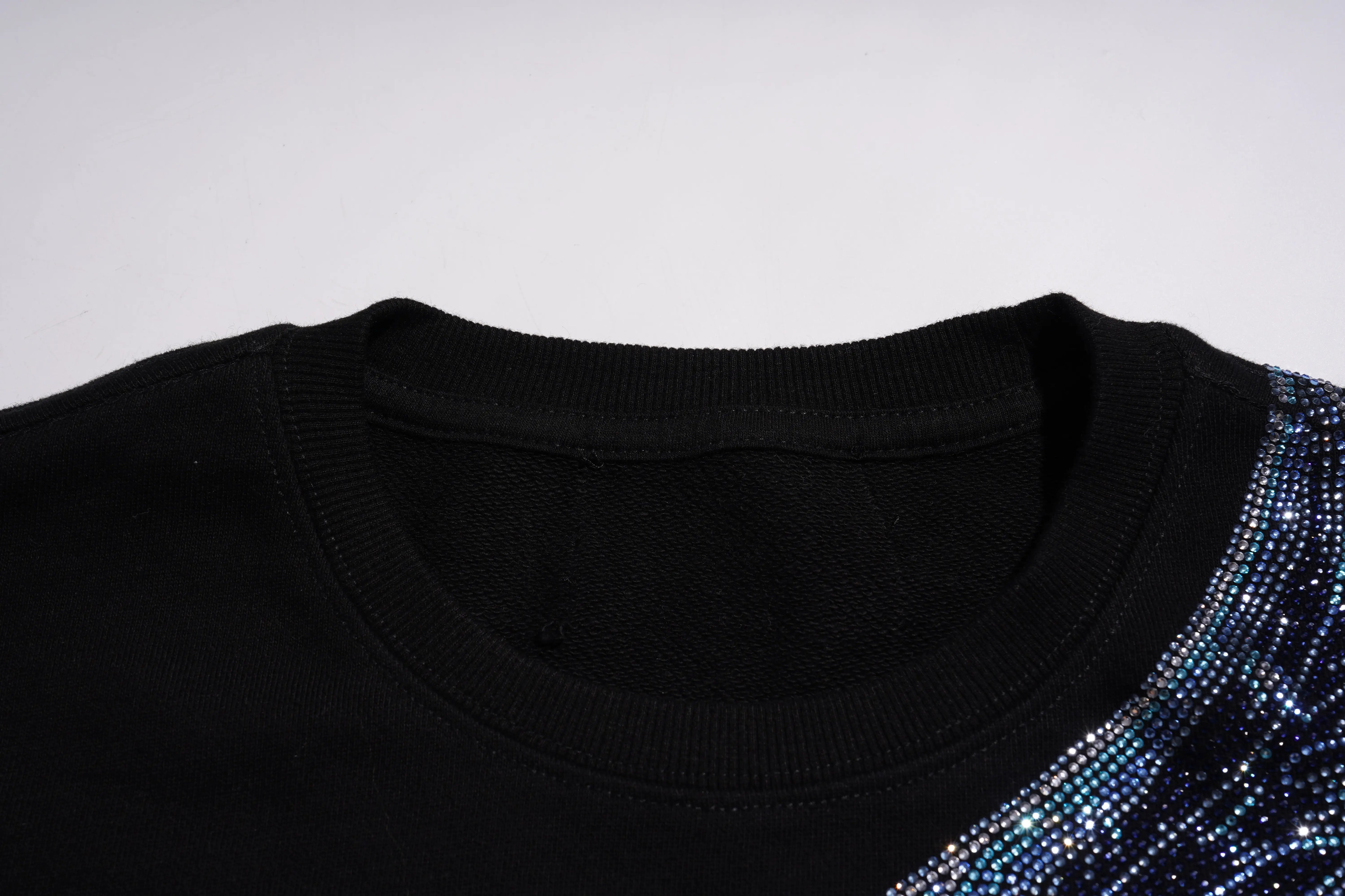 Close-up of a black garment with blue sequins on a white background, TCH Rhinestone Wing Black Crewneck Sweatshirt