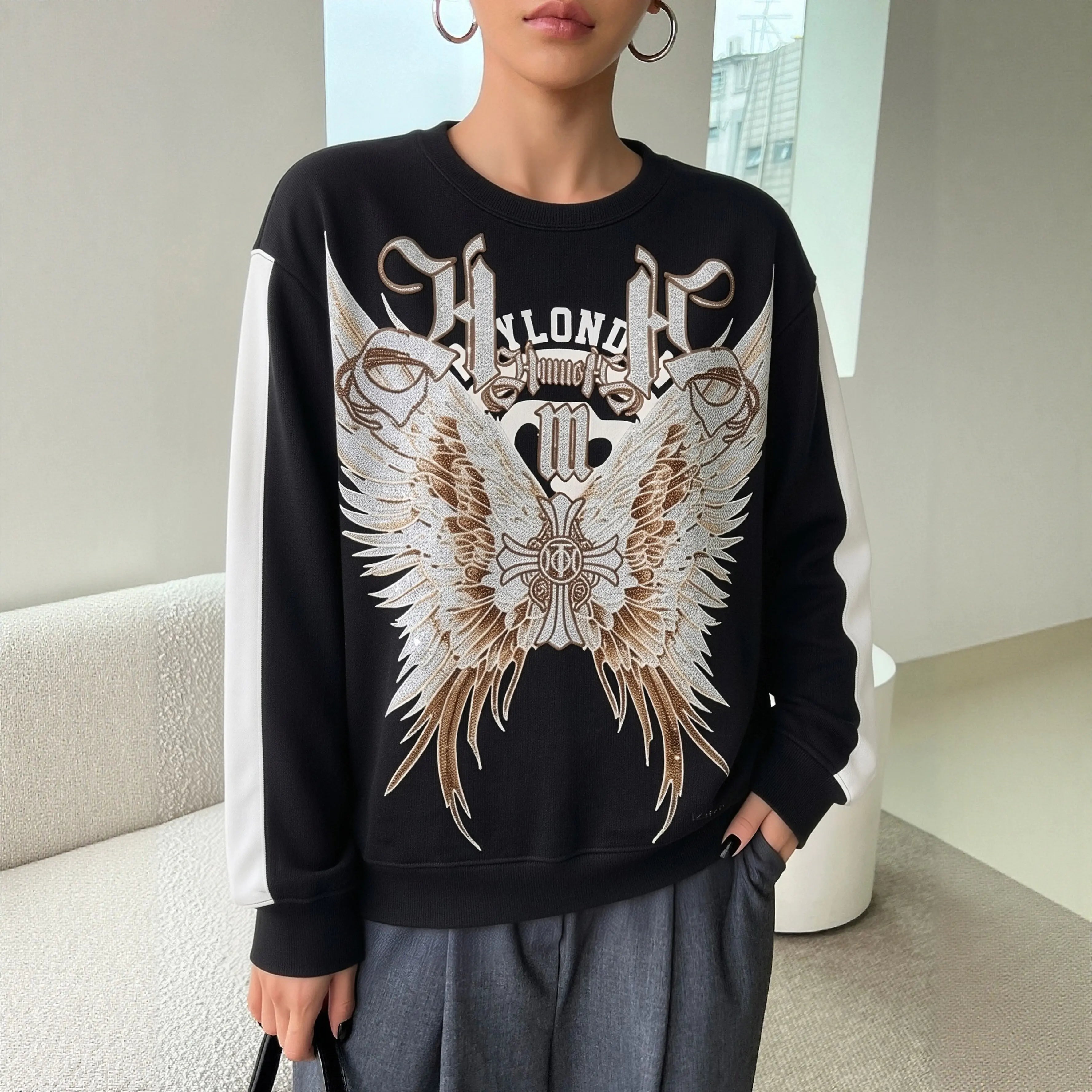 Person wearing a black sweatshirt with a large white and brown graphic design indoors. TCH Rhinestone Wing M Embroidered Sweatshirt