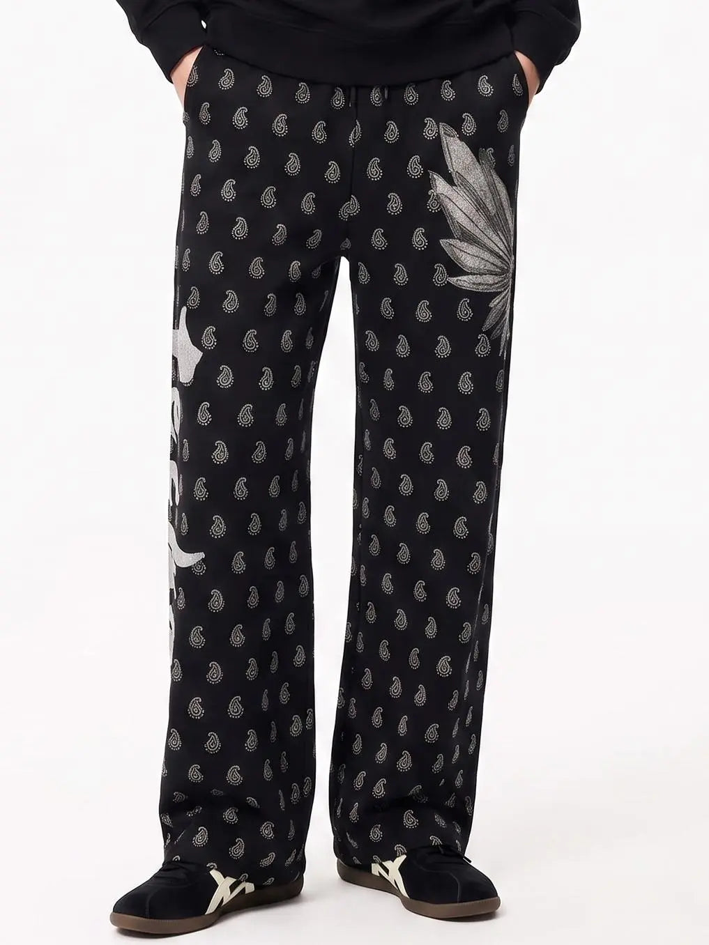 Black wide-leg pajama pants with a silver paisley print and a large silver leaf motif on the right leg, modeled with a black top and black slip-on shoes against a white background. TCH Rhinestone Wing Paisley Wide-Leg Sweatpants