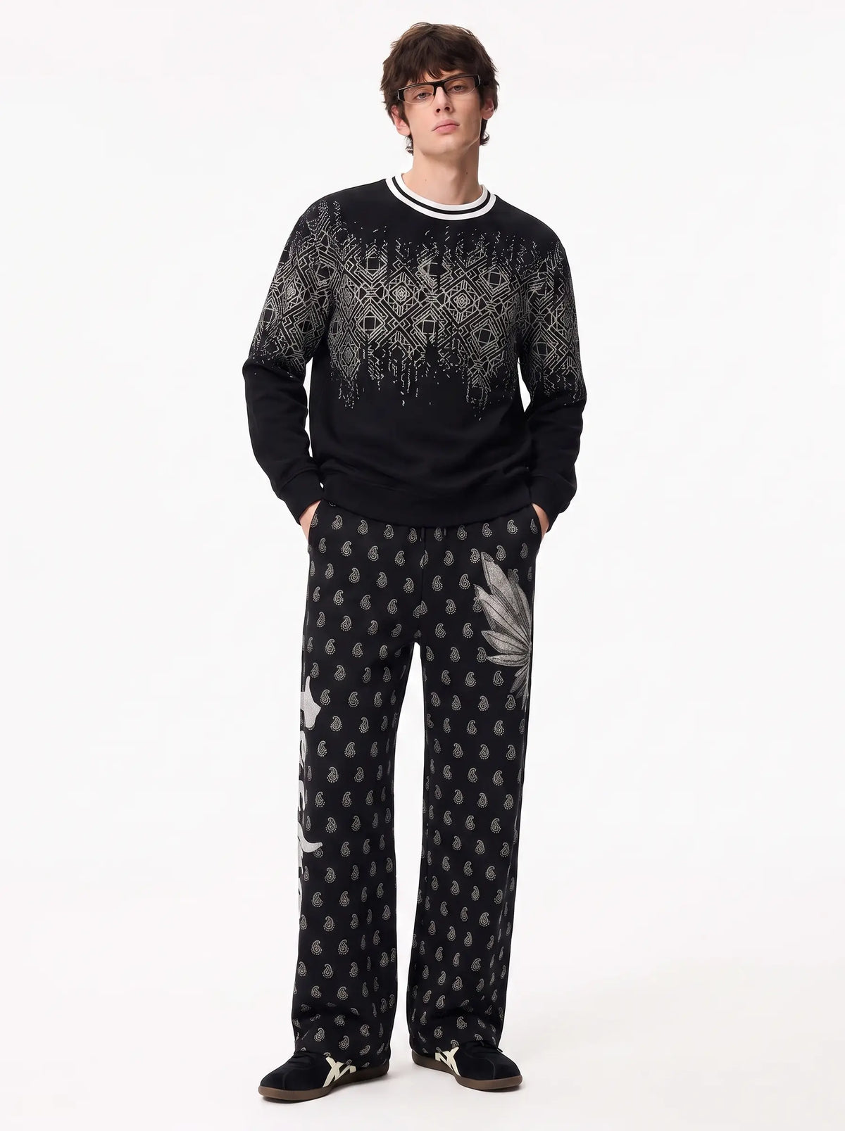 A man modeling a black knit sweater and matching wide-leg trousers with white and gray abstract patterns, photographed against a plain white studio background. TCH Rhinestone Wing Paisley Wide-Leg Sweatpants