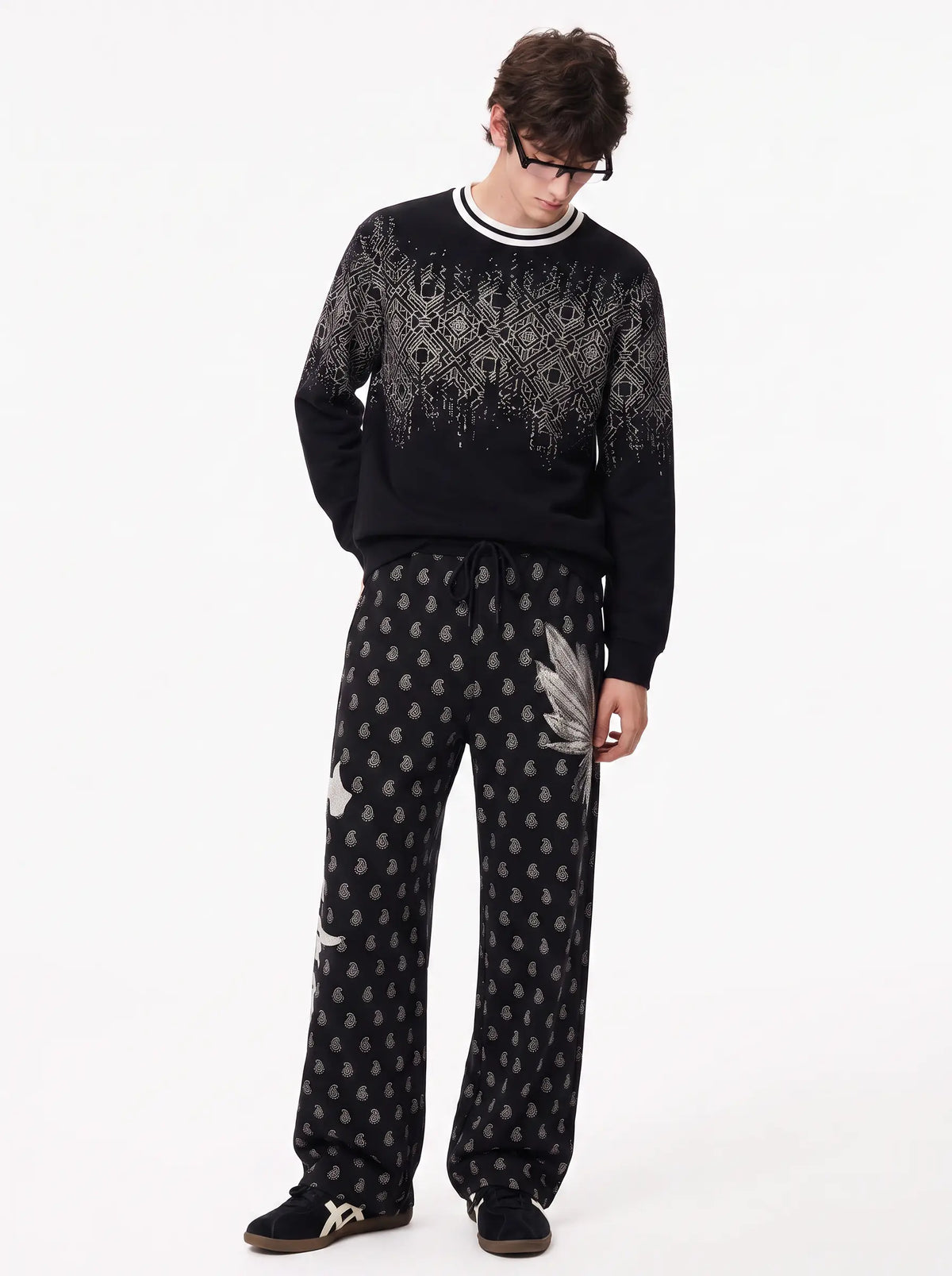 A model wearing a black knit crewneck sweater with a gray geometric pattern on the upper chest and sleeves, paired with matching black and gray patterned sweatpants, against a plain white studio background. TCH Rhinestone Wing Paisley Wide-Leg Sweatpants