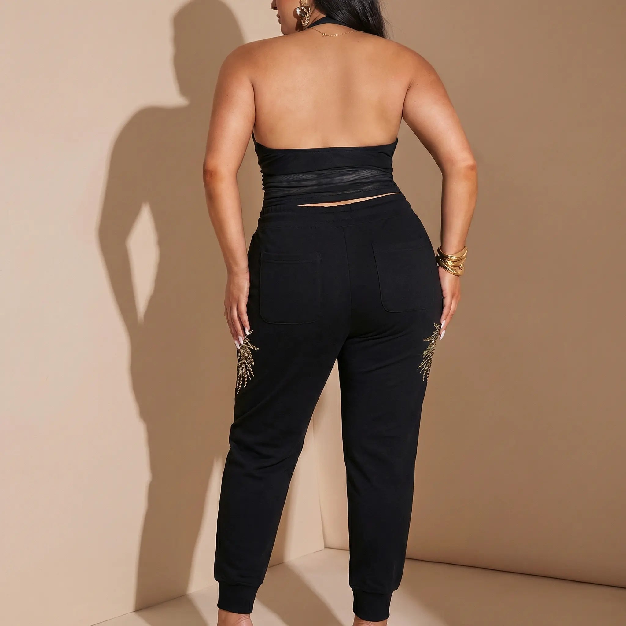 Person wearing a black strapless top and black jogger pants against a beige wall. TCH Rhinestone Wing Techno Jogger Pants