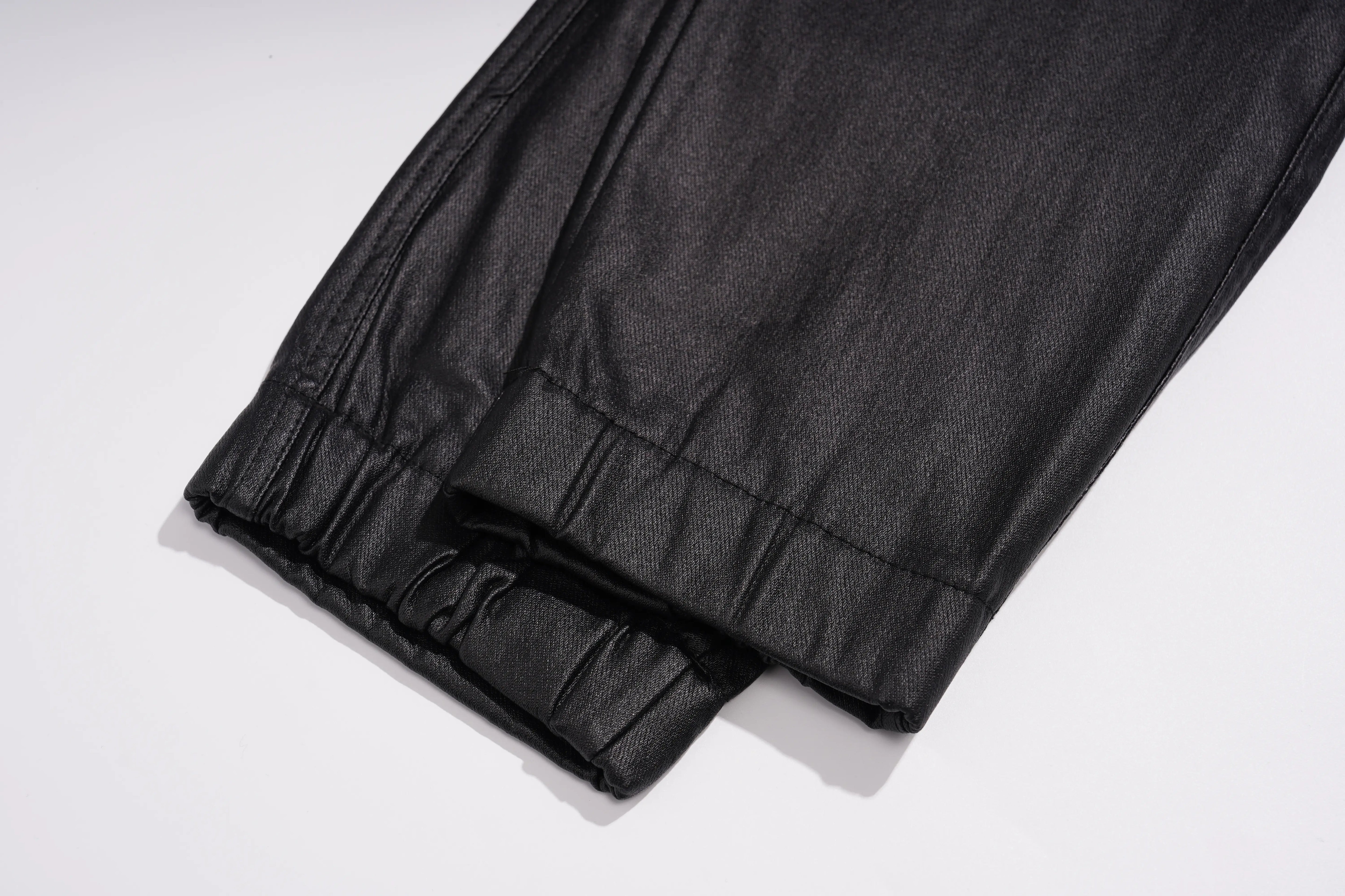 Close-up of a black textured fabric garment, showing a gathered cuff or hem detail on a plain white background. TCH Rhinestone Wing Teddy Faux Leather Jogger Pants