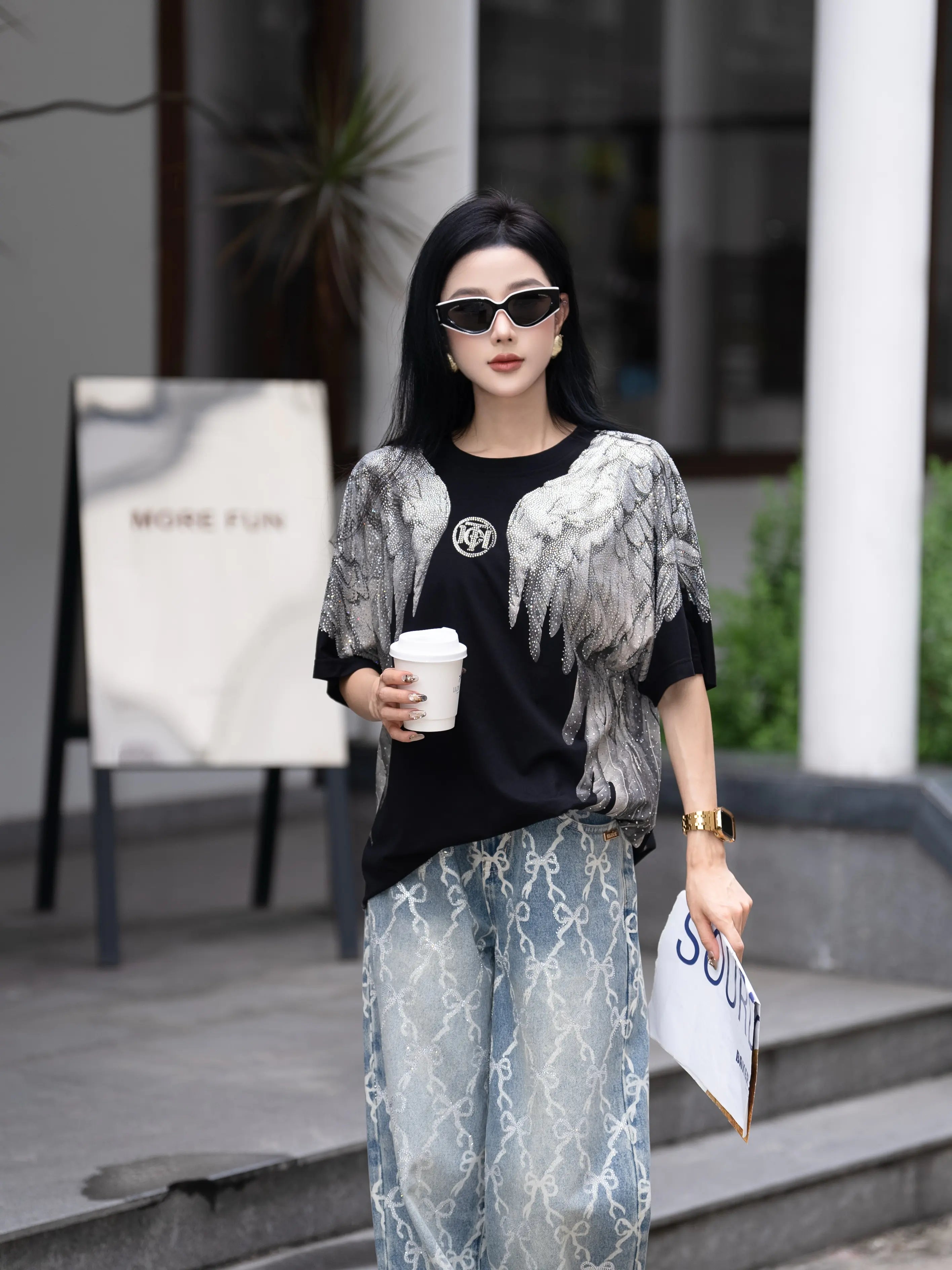 Woman in stylish outfit holding a coffee cup and a magazine outdoors. TCH Rhinestone Wings Logo Black Graphic T-Shirt