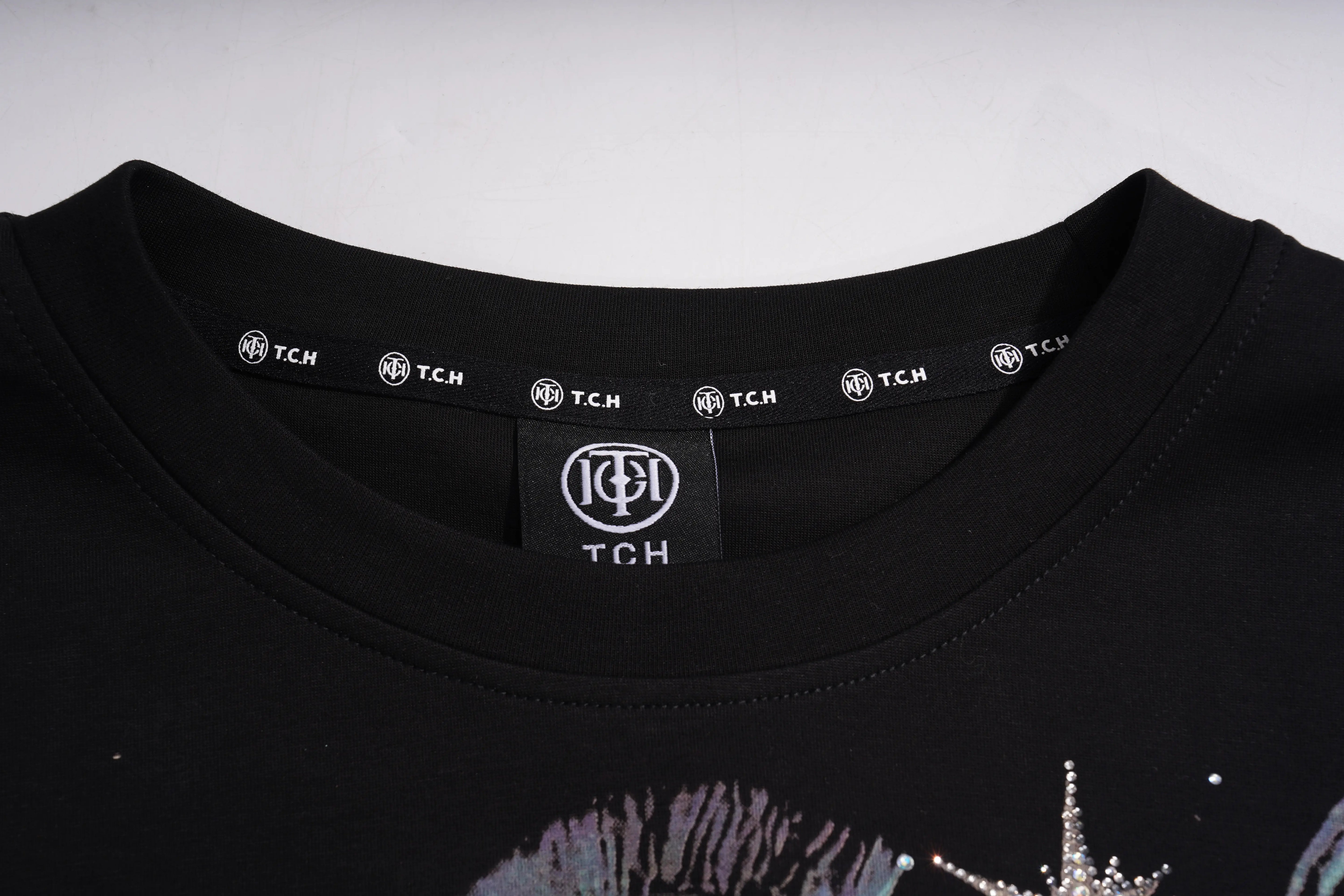 Close-up of a black TCH crewneck t-shirt showing the inner neck label with the brand logo and a partial graphic print on the chest. TCH Sagittarius Celestial Graphic Oversized T-Shirt