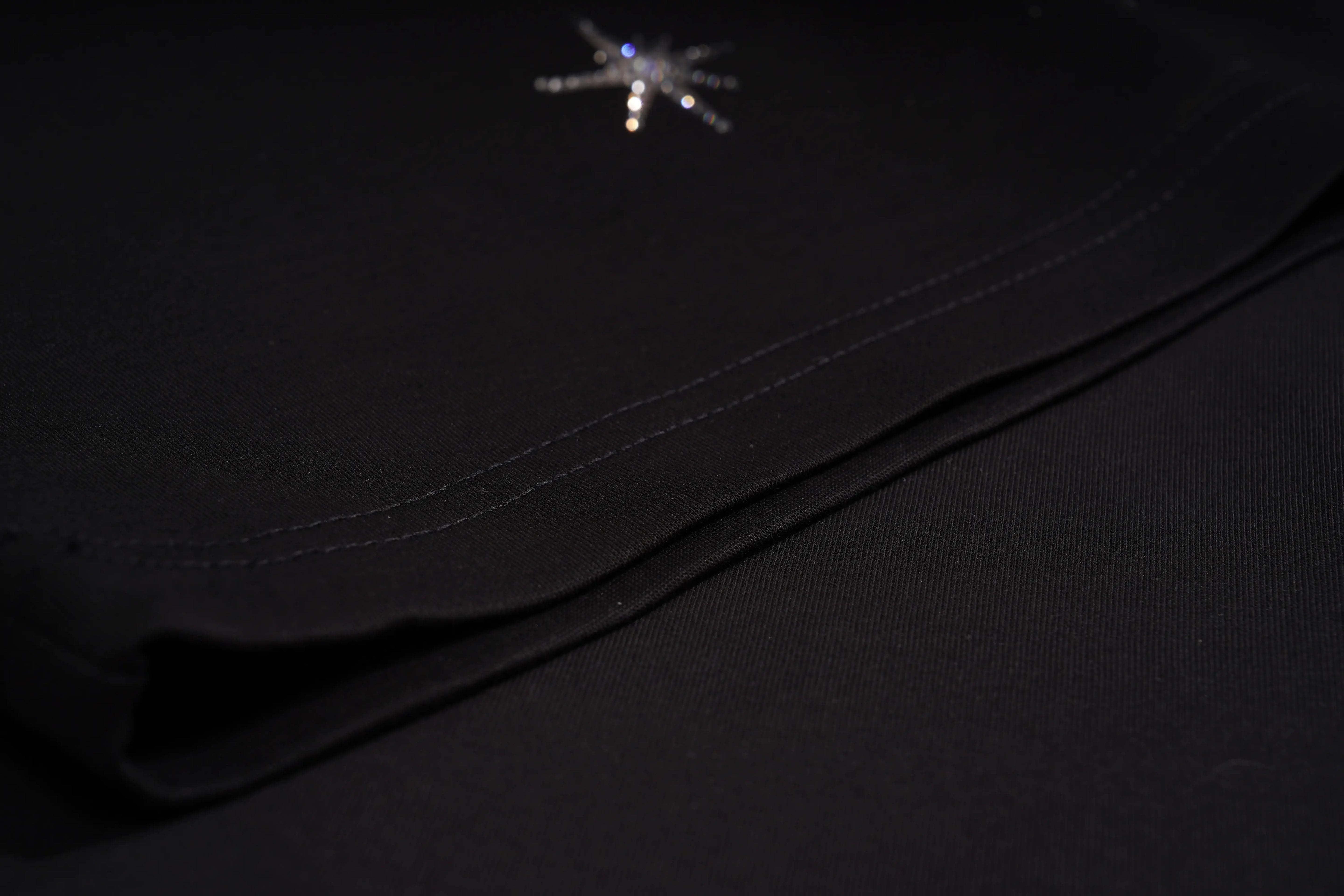 Close-up of a black fabric garment, likely a skirt or dress, showing a diagonal fold with a small silver rhinestone spider brooch near the top. TCH Sagittarius Celestial Graphic Oversized T-Shirt