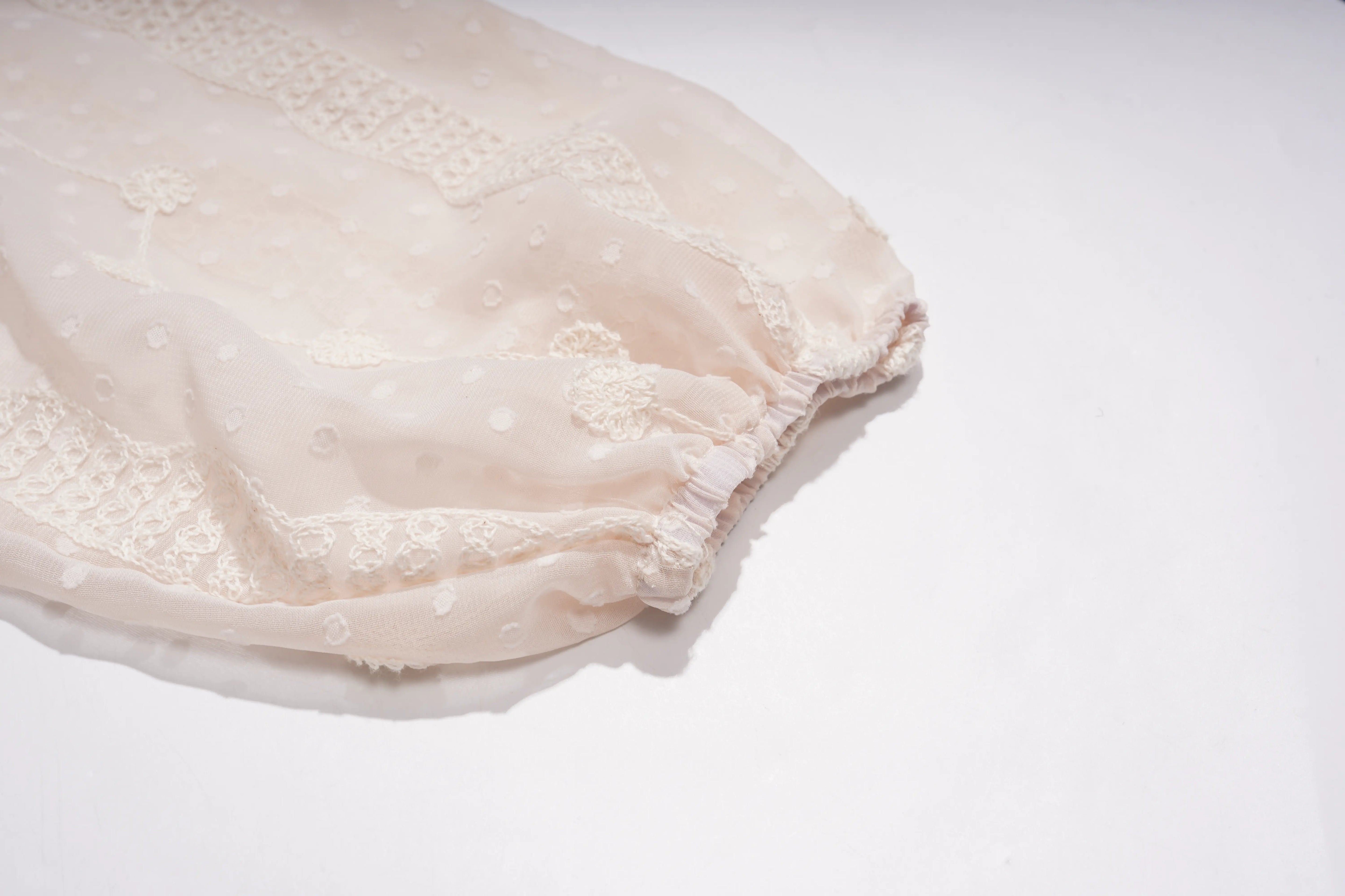 A close-up of a light cream or off-white sheer fabric accessory, possibly a bonnet or soft garment piece, featuring embroidered floral details and a ruffled elastic edge, set against a plain white background. TCH Sheer Rhinestone Angel Star Zip-Up Hoodie