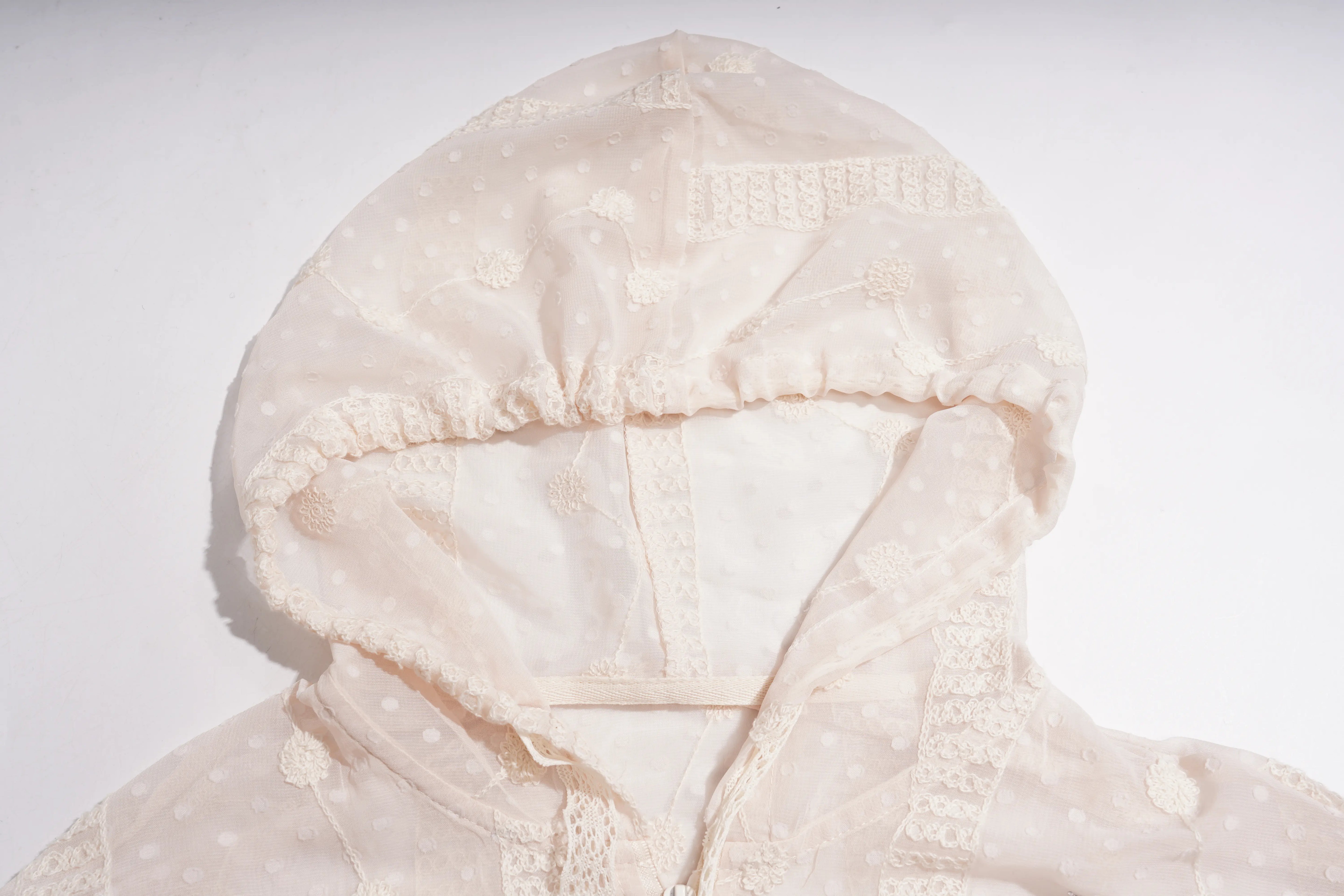 A close-up of a cream-colored hooded garment, likely a baby jacket or bonnet, featuring a sheer polka-dot fabric, lace trim, and a gathered elastic hood on a plain white background. TCH Sheer Rhinestone Angel Star Zip-Up Hoodie