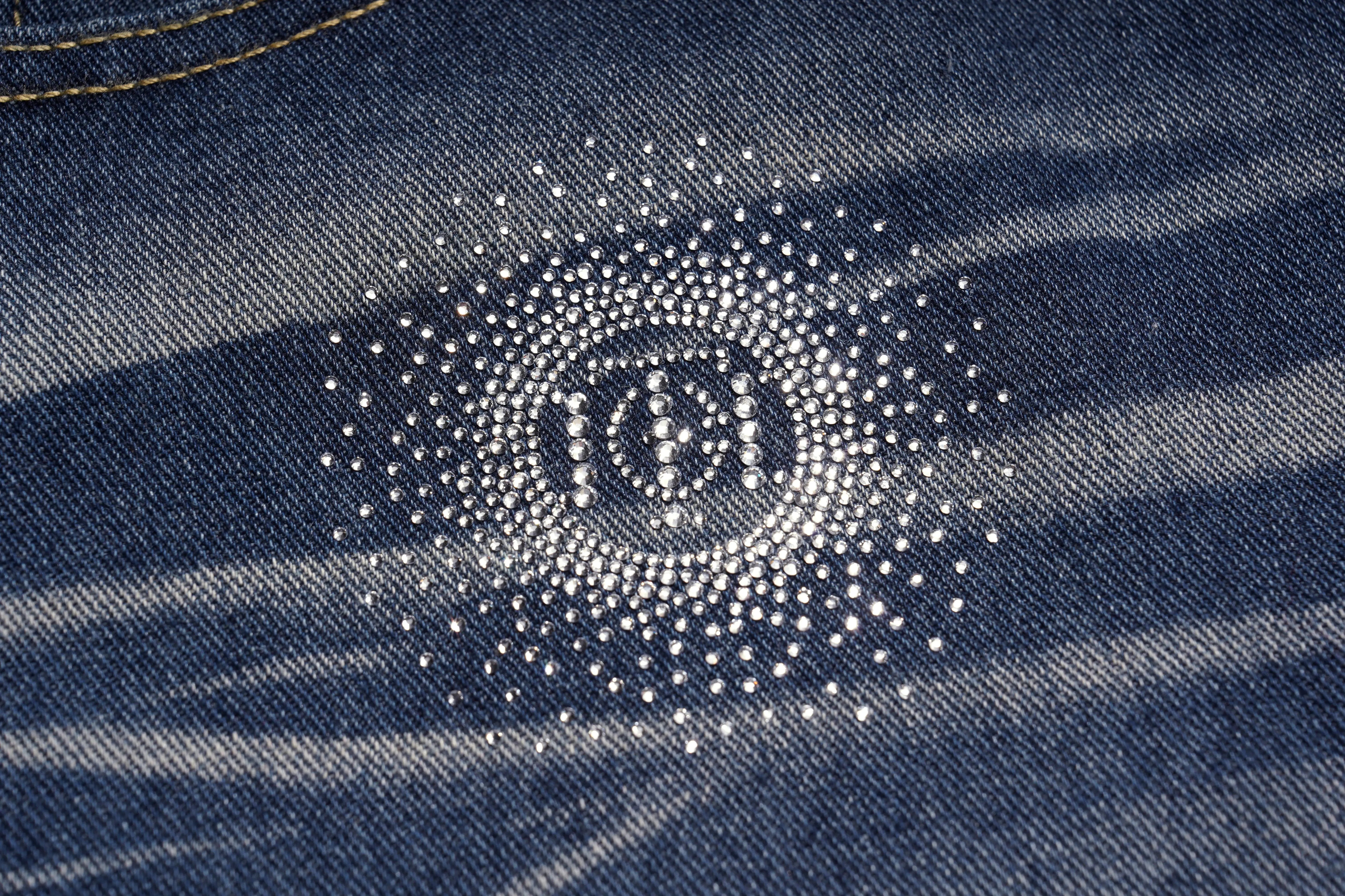 Close-up of a Chanel logo on denim fabric with rhinestones. TCH Shooting Star Rhinestone Wide-Leg Blue Jeans
