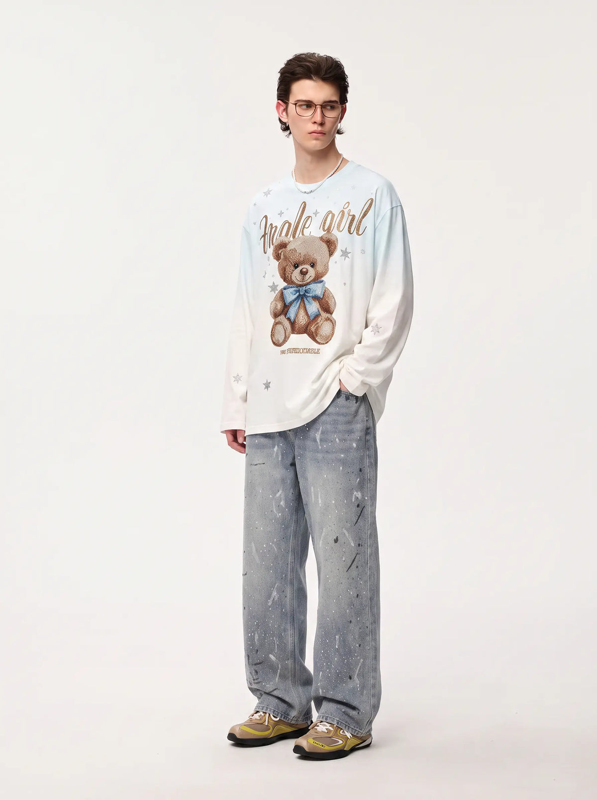 A model stands against a plain light background wearing a cream long-sleeve graphic sweatshirt with a teddy bear print and the words 'make a girl', paired with light blue distressed jeans and gold sneakers. TCH Small Bear Angel Wings Rhinestone Graphic White Long Sleeve T-Shirt