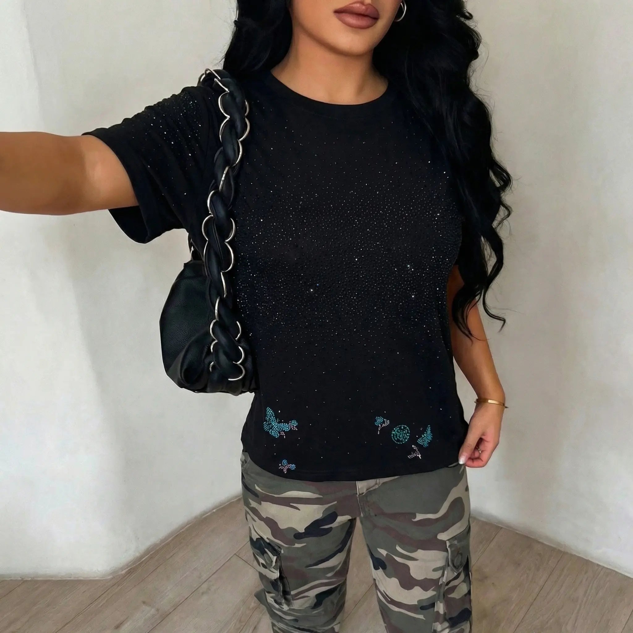 Person wearing a black t-shirt with sequins and camouflage pants, holding a black handbag. TCH Starry Gradient Rhinestone Butterfly T-Shirt