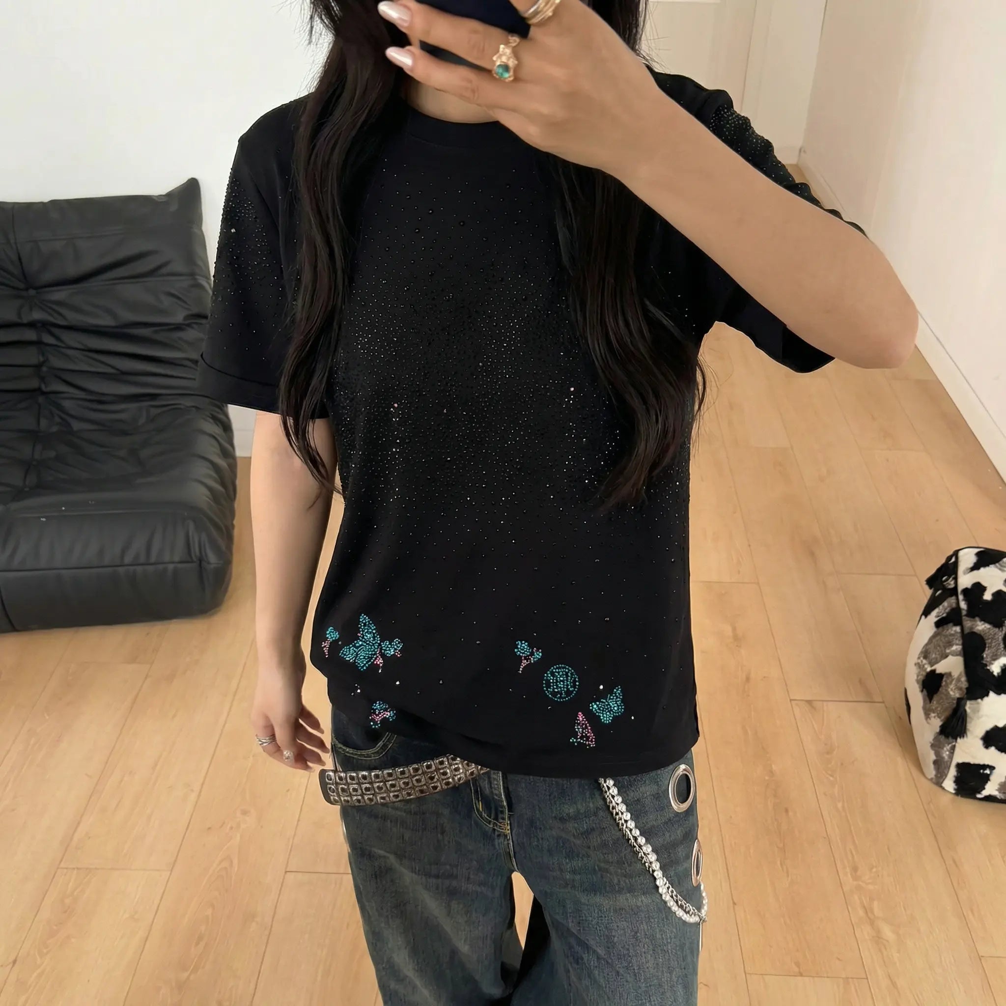 Person wearing a black t-shirt with colorful designs in a room with a black couch and wooden floor. TCH Starry Gradient Rhinestone Butterfly T-Shirt