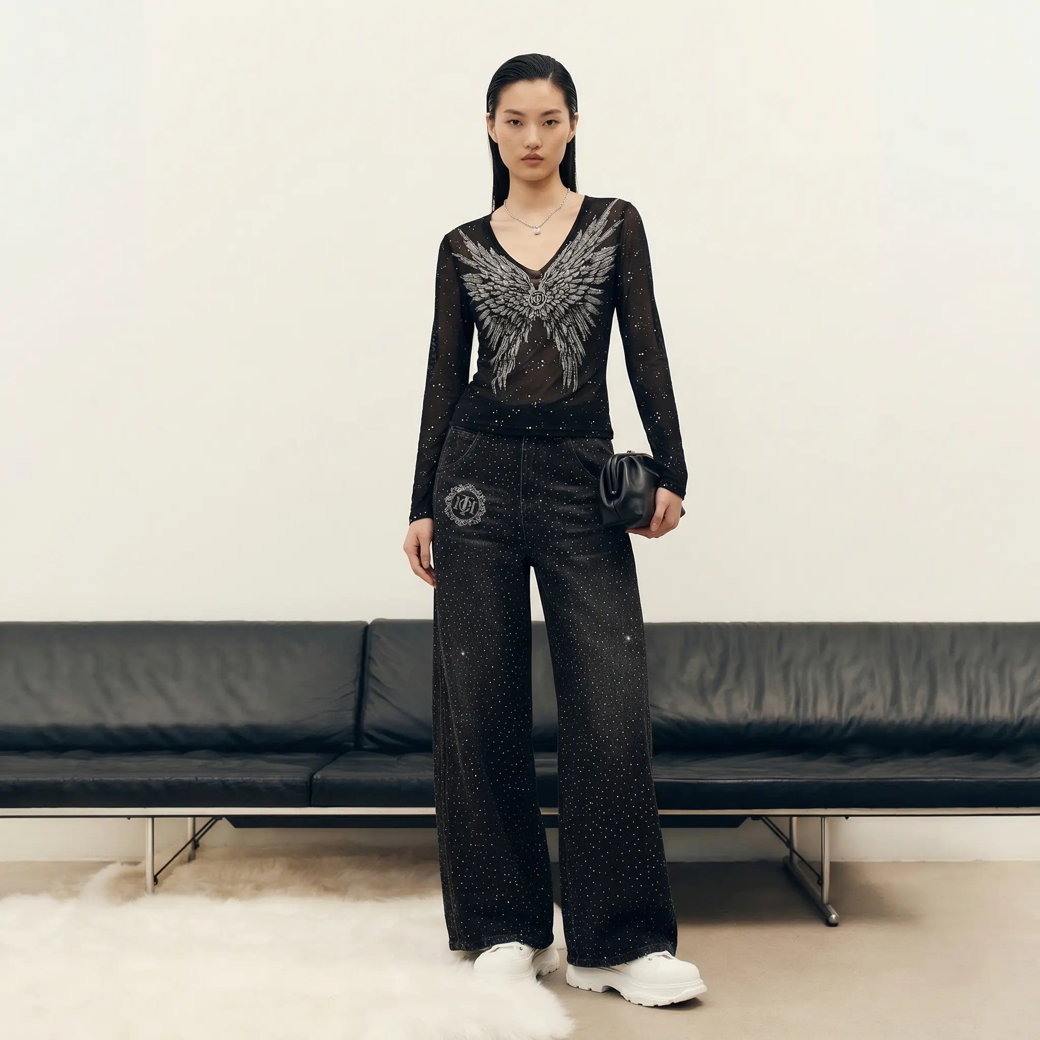 Model wearing a black outfit with silver embellishments in a minimalistic setting. TCH Starry Rhinestone Logo Black Denim Jeans