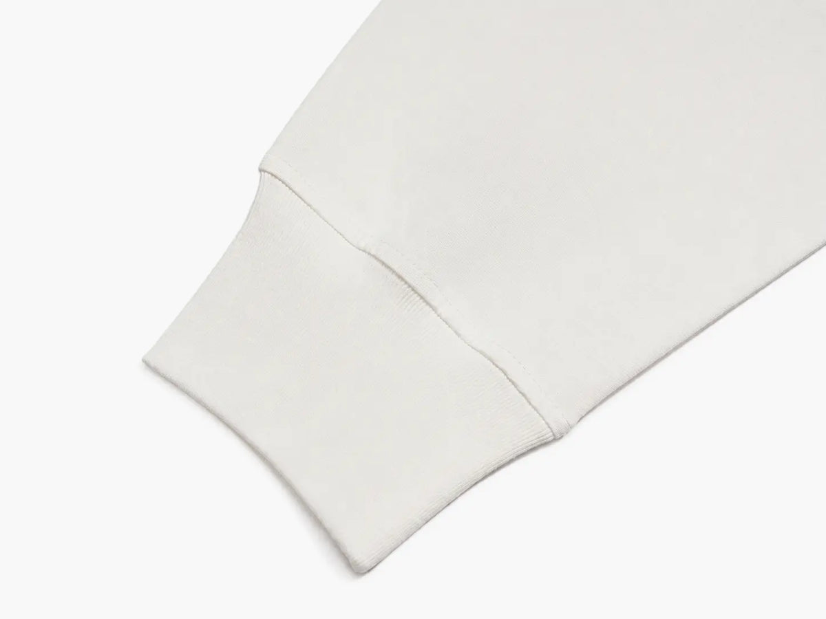 Close-up of a light cream or off-white fabric cuff with a clean, folded hem and fine ribbed texture, set against a solid white background. TCH Starry Western Graphic White Long Sleeve Top
