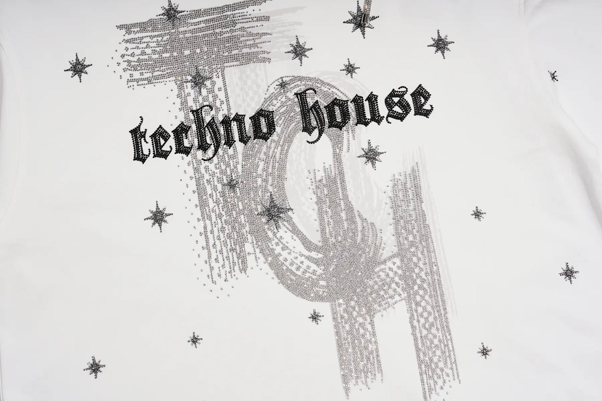 White t-shirt featuring a silver glitter graphic of a stylized 'T' and 'H' with the gothic text 'techno house' printed across the chest, surrounded by small silver star accents. TCH Starry Western Graphic White Long Sleeve Top
