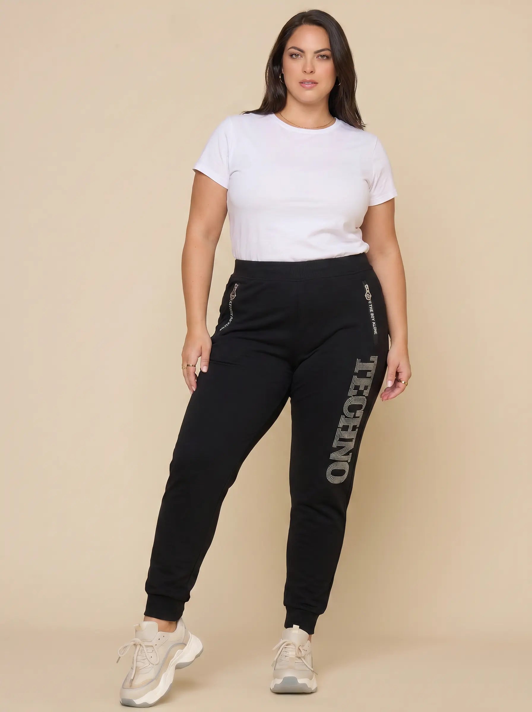 Woman wearing black jogger pants with 'Tekno' branding on a beige background, TCH TECHNO Rhinestone Jogger Pants
