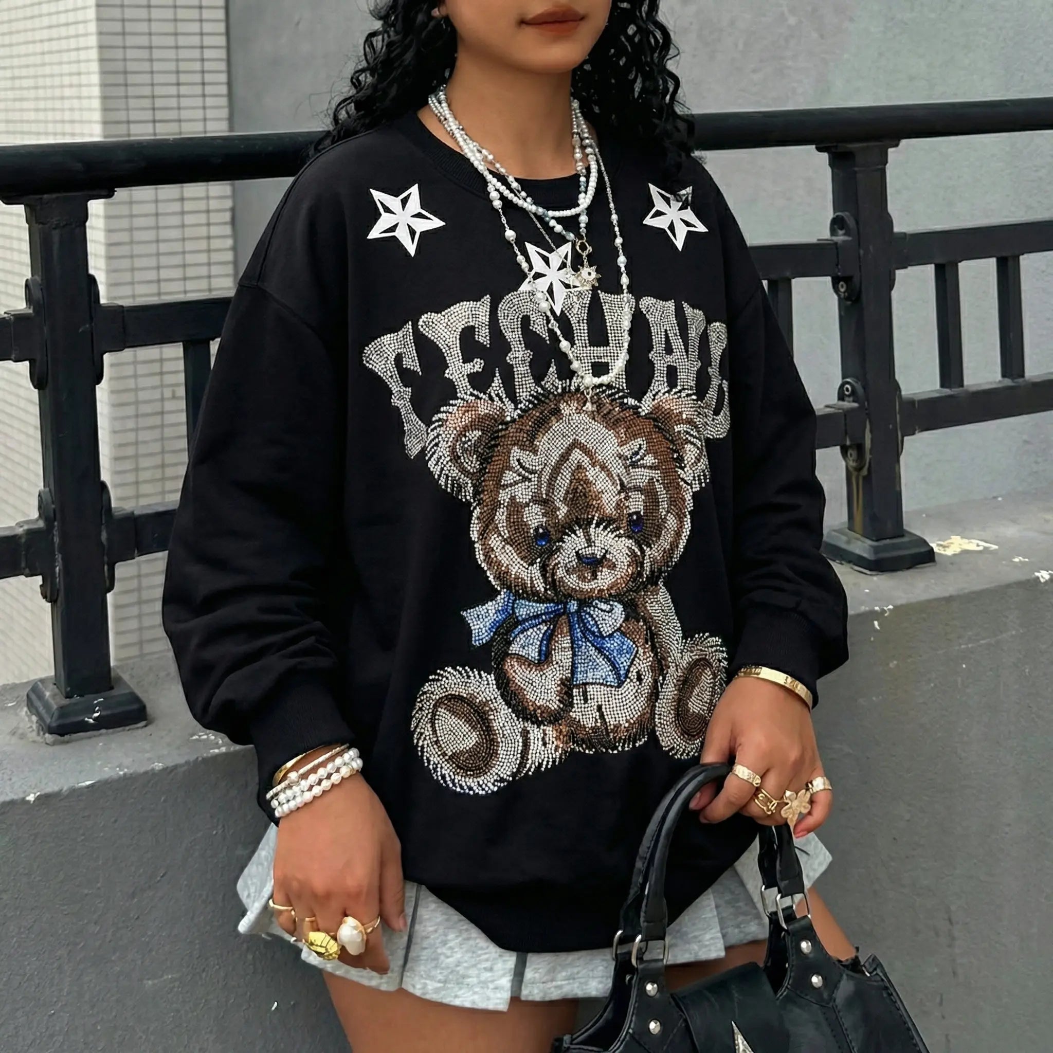 Person wearing a black sweatshirt with a teddy bear graphic and 'FEEL CALM' text, standing against a gray wall. TCH TECHNO Rhinestone Teddy Sweatshirt