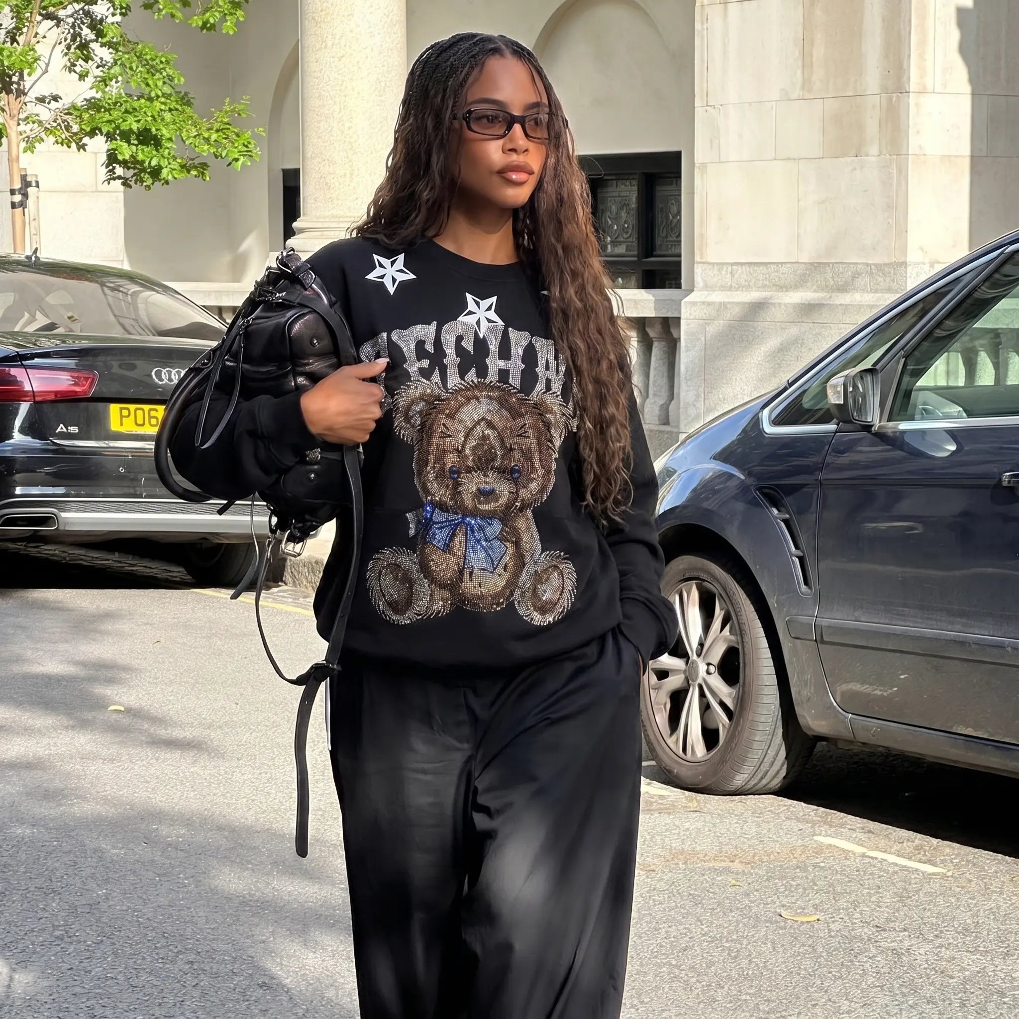 Woman wearing a black sweater with a teddy bear design, standing on a street.TCH TECHNO Rhinestone Teddy Sweatshirt