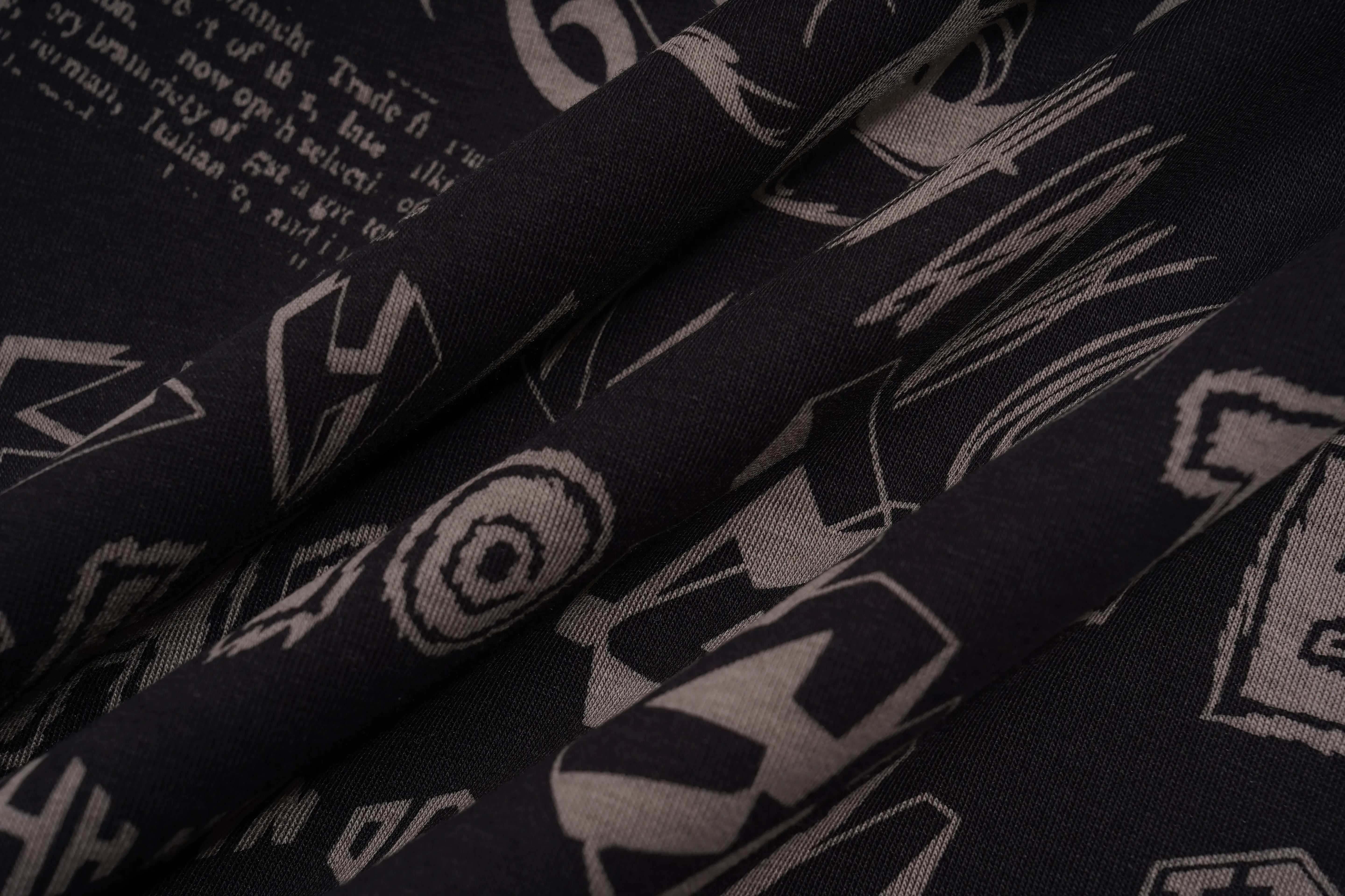 Black fabric with a white graphic pattern of stylized letters and text, shown in soft folds. TCH Techno Graffiti Rhinestone Skull Oversized T-Shirt