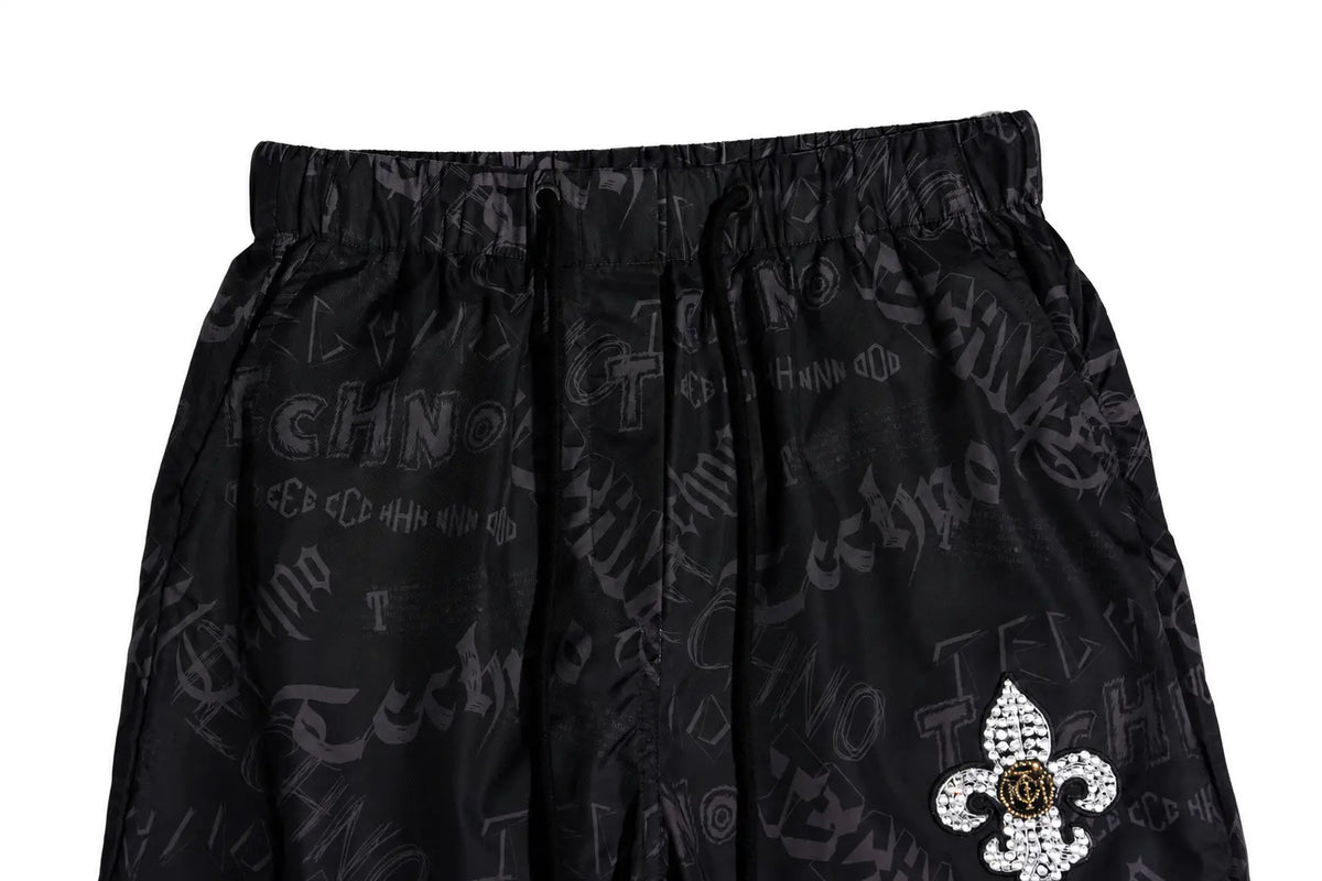 Black athletic shorts featuring an all-over gothic-style script print and a rhinestone-embellished fleur-de-lis patch on the lower left leg. TCH Techno Logo Wide-Leg Cargo Pants