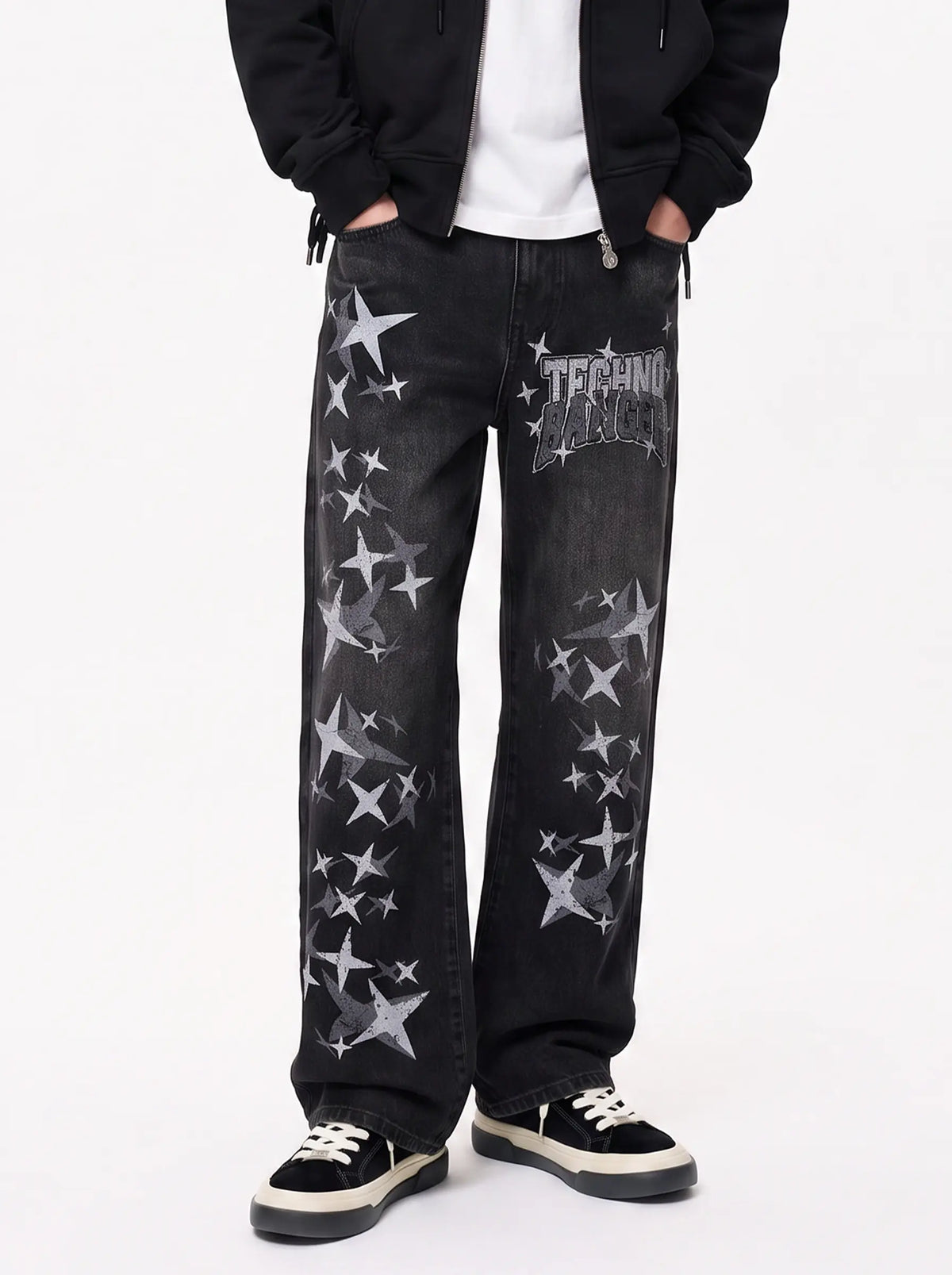 A person wearing black wide-leg jeans with distressed silver star graphics and a metallic 'TECHNIQUE' logo patch on the thigh, styled with a black jacket, white t-shirt, and black sneakers. TCH Techno Magic Star Graphic Wide-Leg Jeans