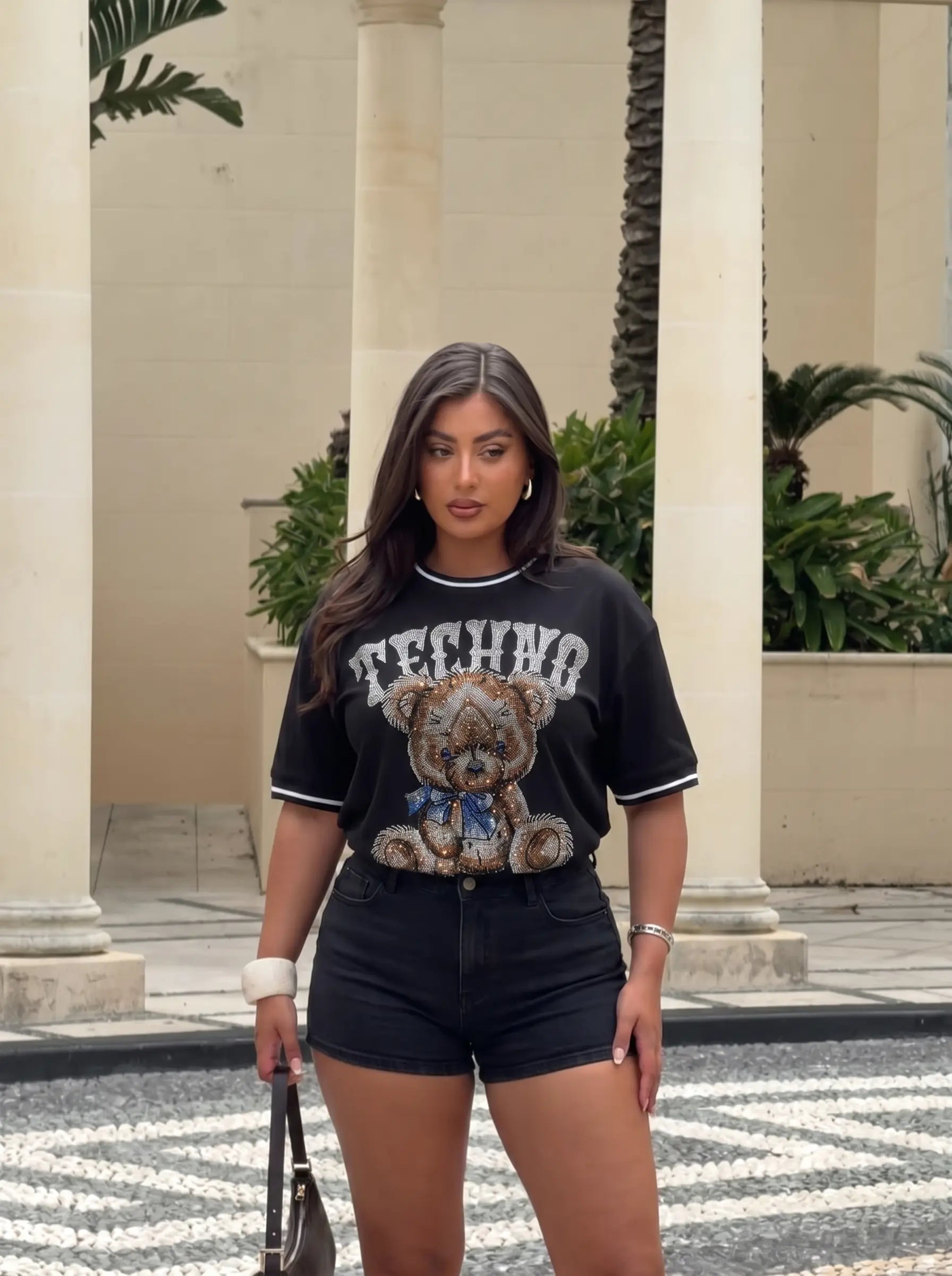 Woman wearing a black t-shirt with a teddy bear graphic and 'FENDI' branding, standing outdoors. TCH Techno Teddy Rhinestone T-Shirt