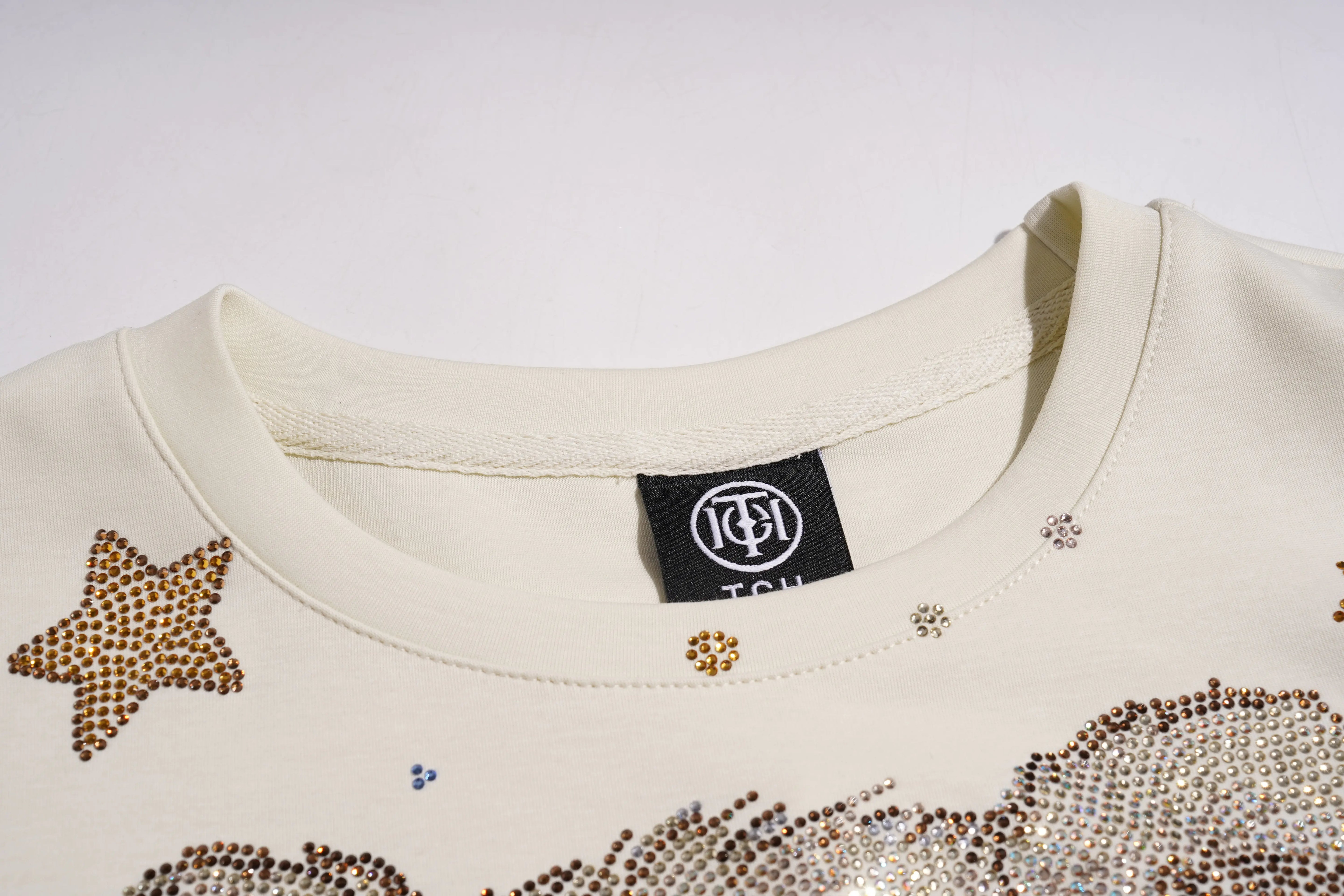Close-up of a cream-colored garment with star-shaped embellishments and a visible brand label. TCH Teddy Bear Garden Rhinestone Lounge Set