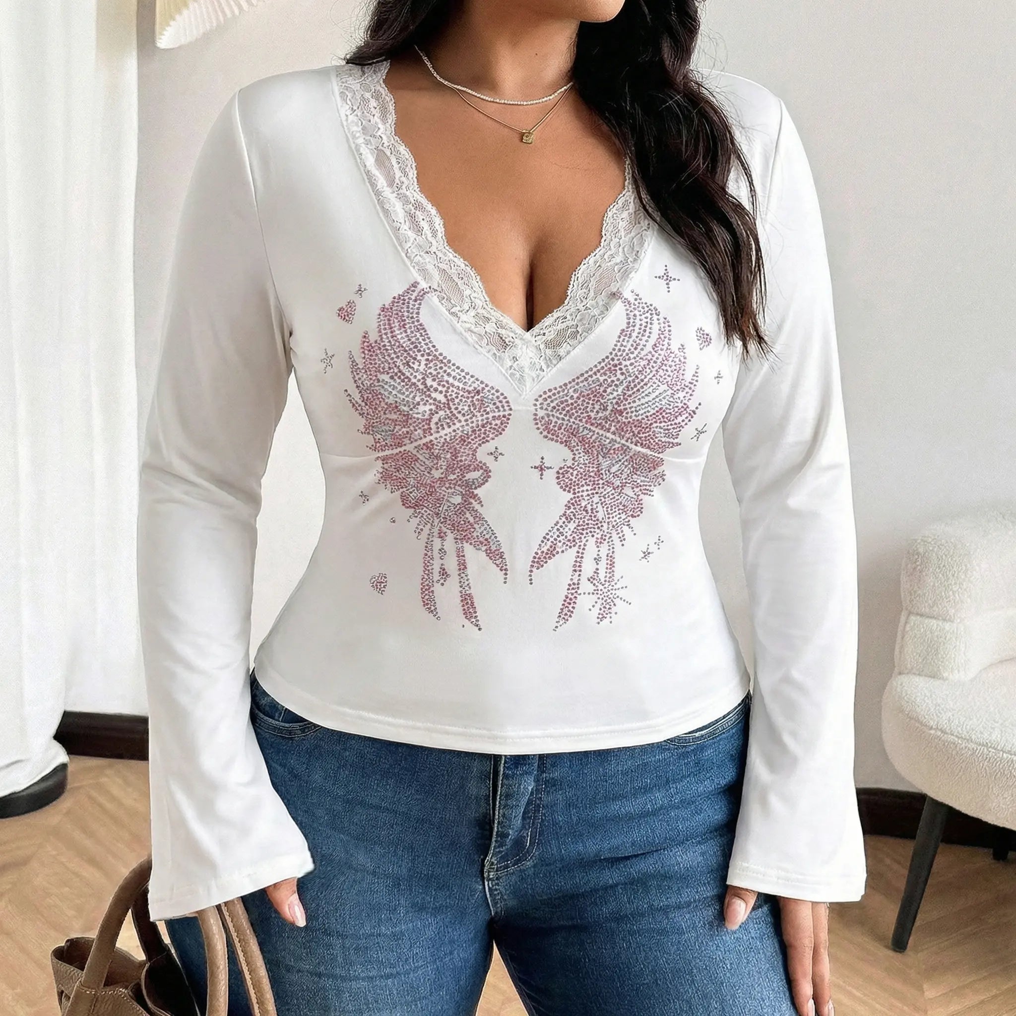 Woman wearing a white long-sleeve top with lace detailing and pink floral design, paired with blue jeans indoors. TCH White Lace Trim V-Neck Rhinestone Wing Long Sleeve Top