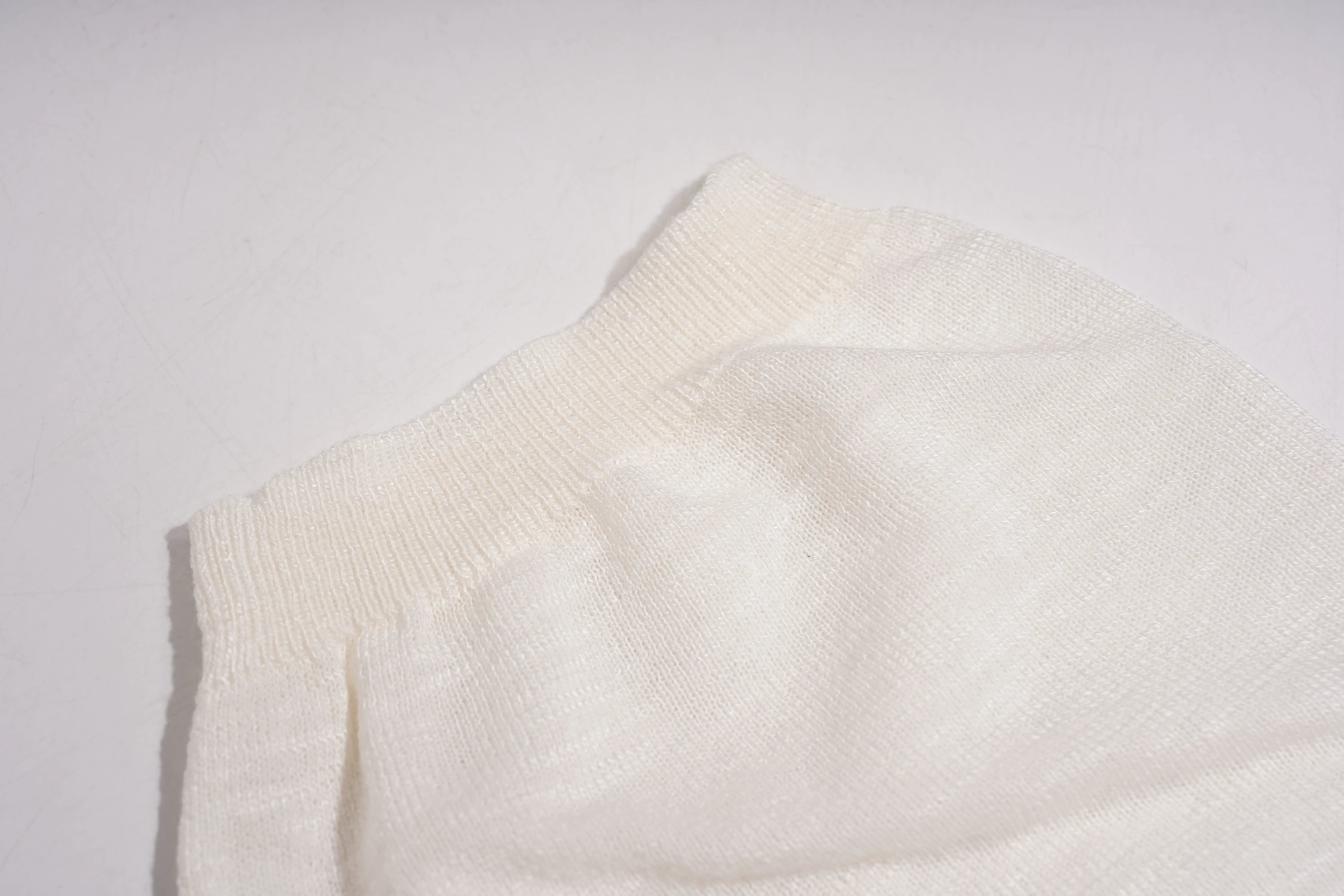 Close-up of a textured white fabric on a light gray background, TCH White Rhinestone Bow Knit Cardigan