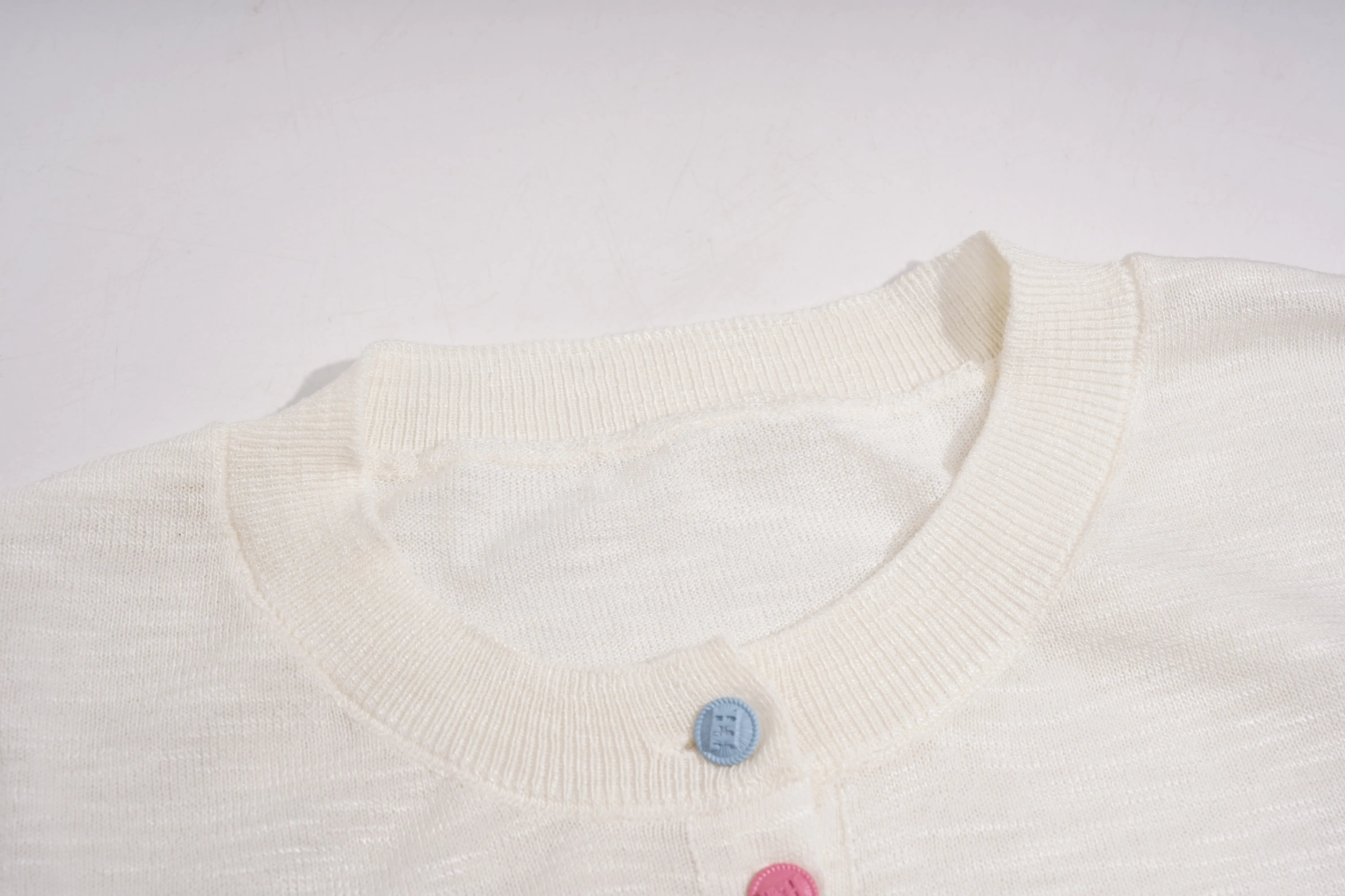 Close-up of a white sweater with colorful buttons on a light gray background, TCH White Rhinestone Bow Knit Cardigan