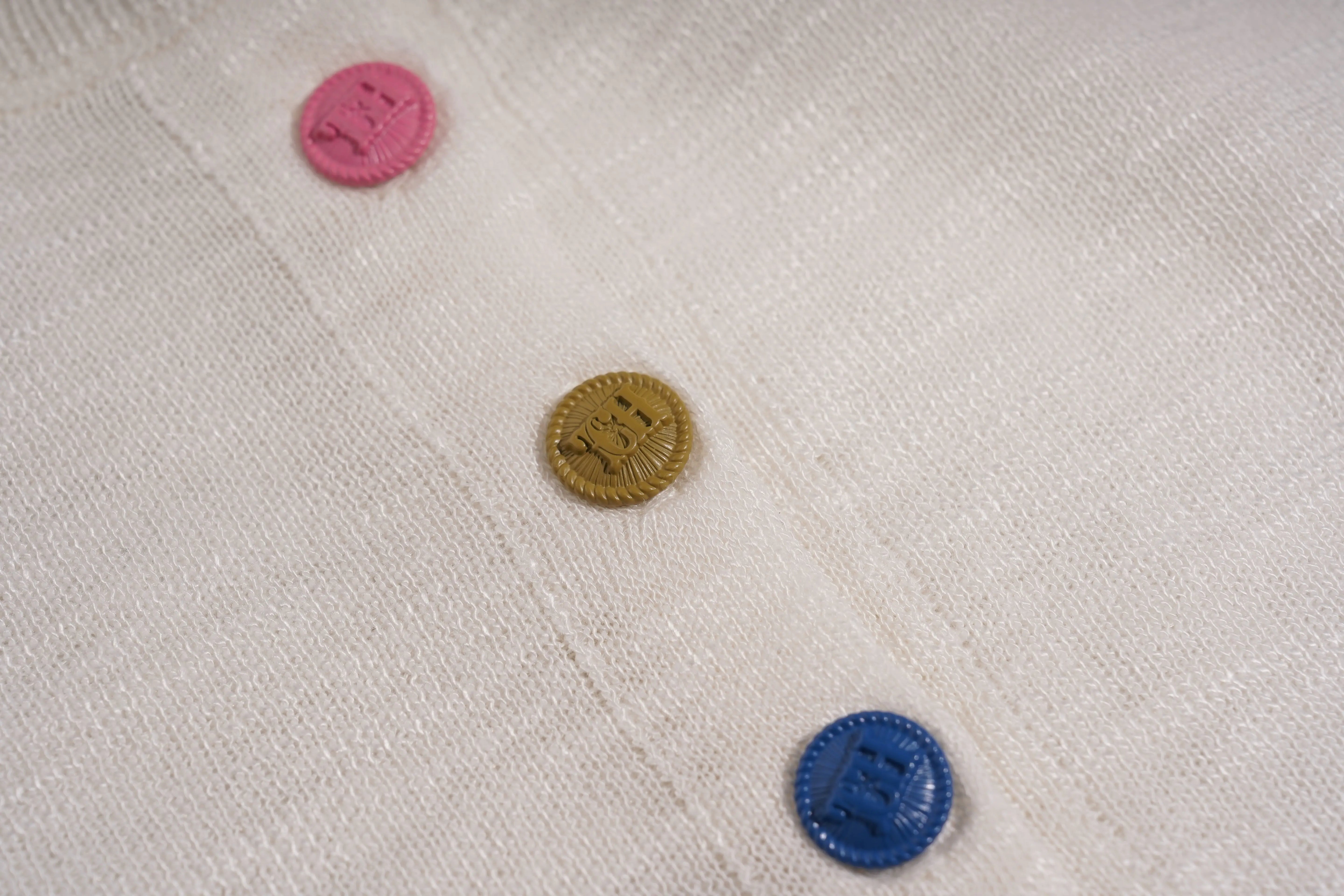 Close-up of three buttons on a textured fabric background, TCH White Rhinestone Bow Knit Cardigan
