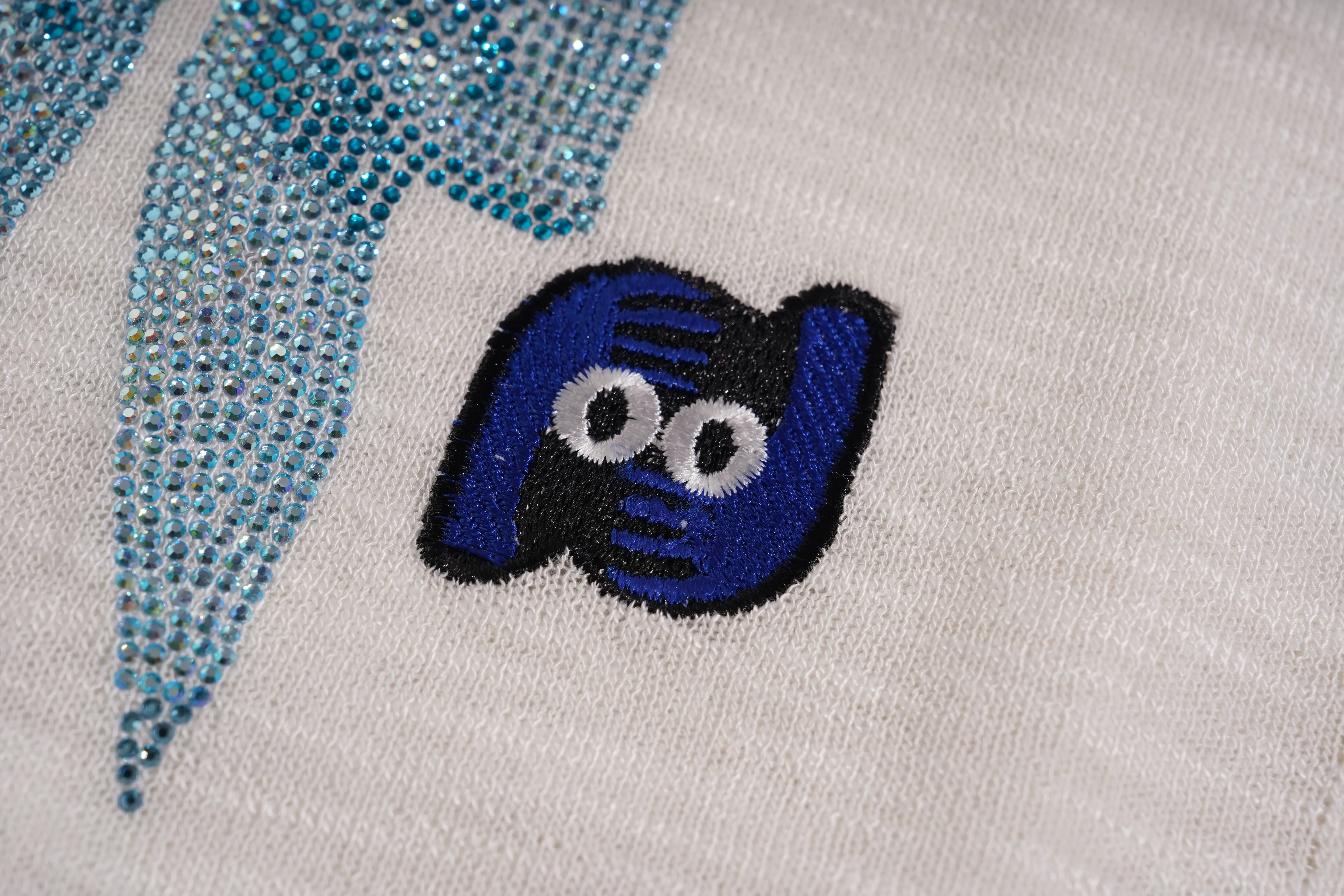 Close-up of a blue and black embroidered design on fabric with a white background, TCH White Rhinestone Bow Knit Cardigan