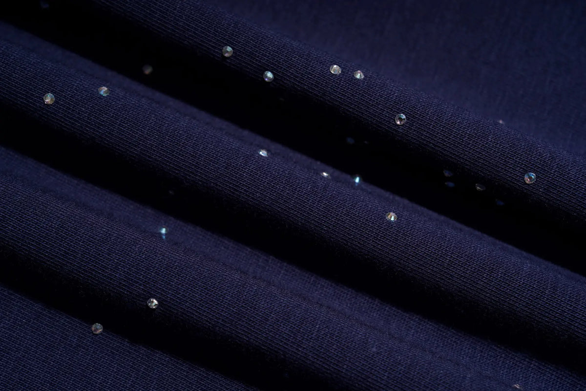 Close-up of dark navy fabric with multiple small iridescent rhinestones or sequins scattered across the surface, shown in soft diagonal folds. TCH Winged Unicorn Starry Rhinestone Long Sleeve T-Shirt