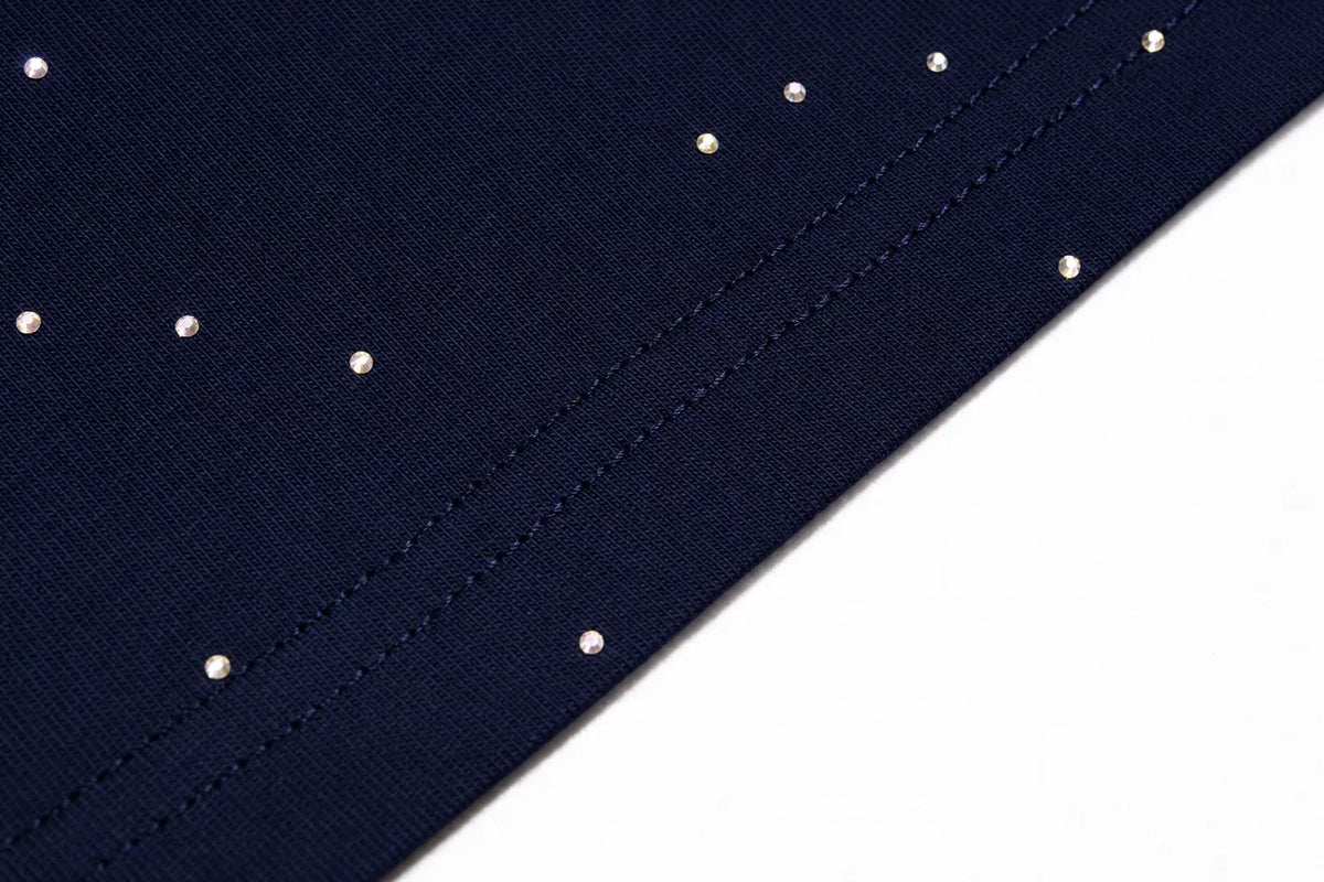 Close-up of a navy blue fabric surface with a diagonal seam and small evenly spaced silver studs or rhinestones on a white background. TCH Winged Unicorn Starry Rhinestone Long Sleeve T-Shirt
