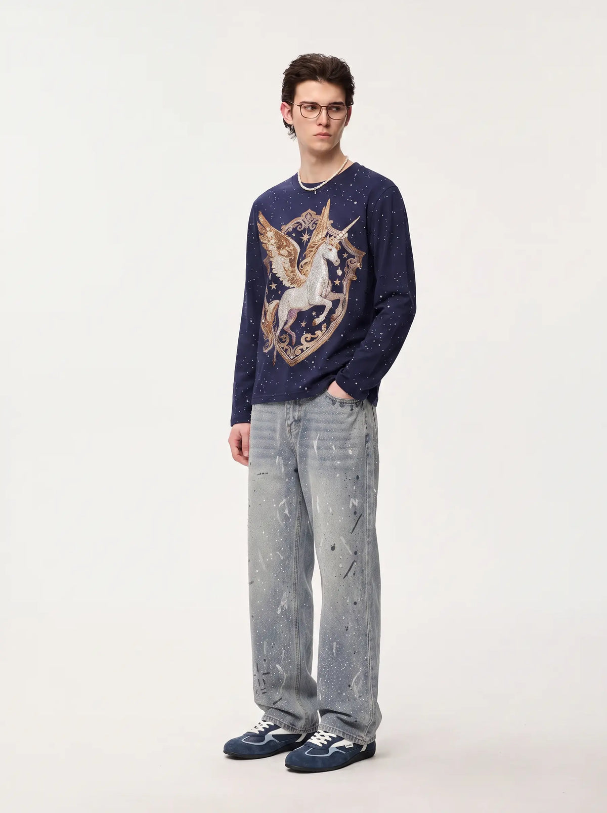 A man wearing a navy blue long-sleeve knit sweater with a large gold and white unicorn graphic on the front, paired with light gray paint-splattered jeans and navy sneakers, standing against a plain off-white studio background. TCH Winged Unicorn Starry Rhinestone Long Sleeve T-Shirt