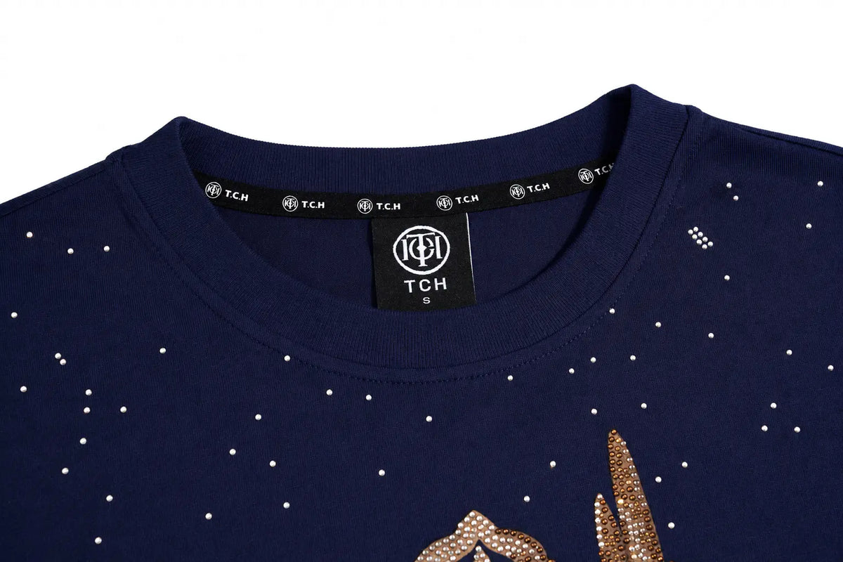 Close-up of a navy blue crewneck sweatshirt with rhinestone star details and a gold rhinestone graphic on the lower front, featuring a black neck label with the TCH brand logo. TCH Winged Unicorn Starry Rhinestone Long Sleeve T-Shirt