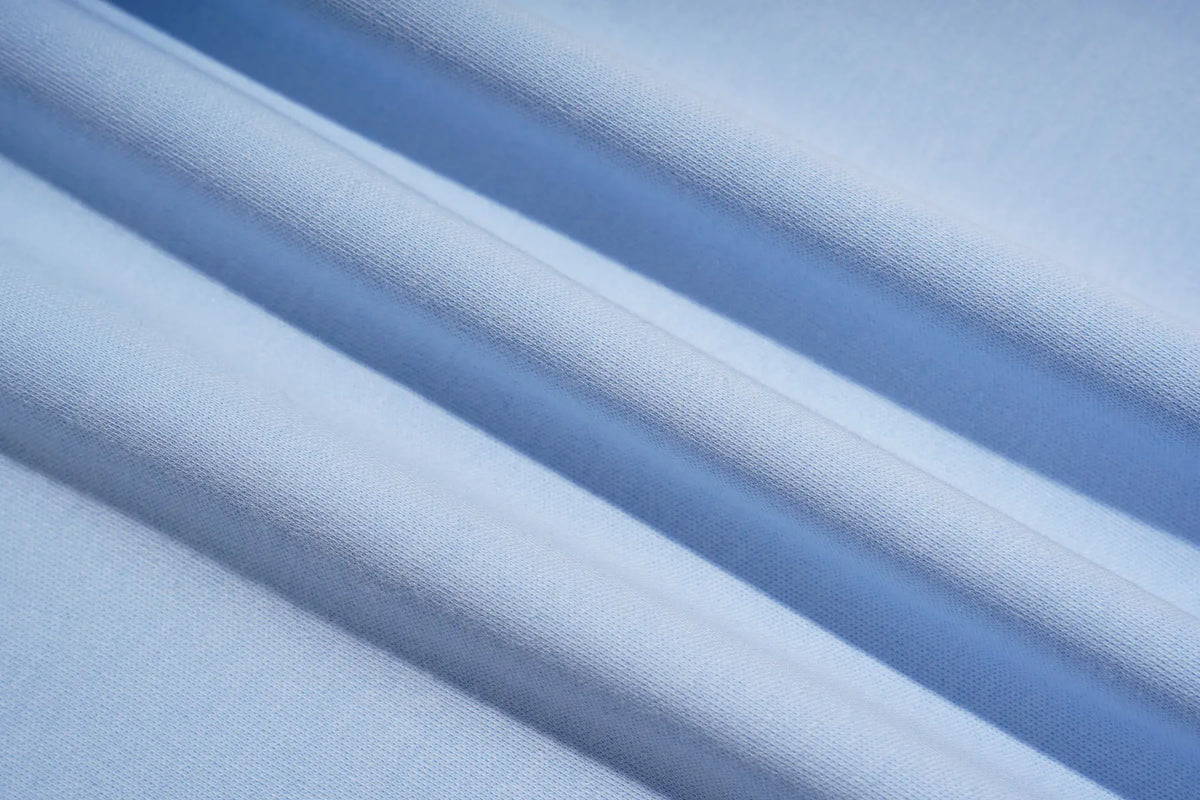 A close-up of light blue fabric with soft diagonal folds and a fine woven texture. TCH Women's Blue Teddy Bear Graphic Oversized T-Shirt